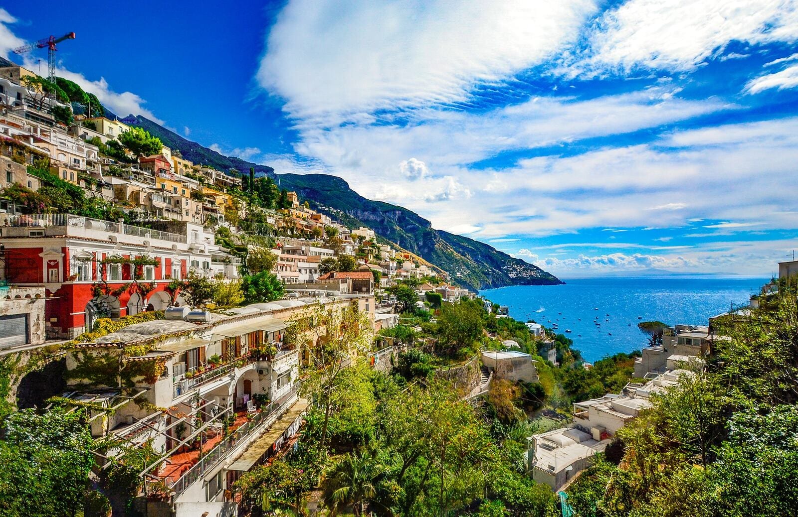 Amalfi Coast's vibrant cliffside buildings cascade towards the azure Tyrrhenian Sea, framed by lush greenery and rugged cliffs under a dramatic sweeping sky, offering a quintessential Italian seaside escape. | Houfy — No Fees, Book Direct