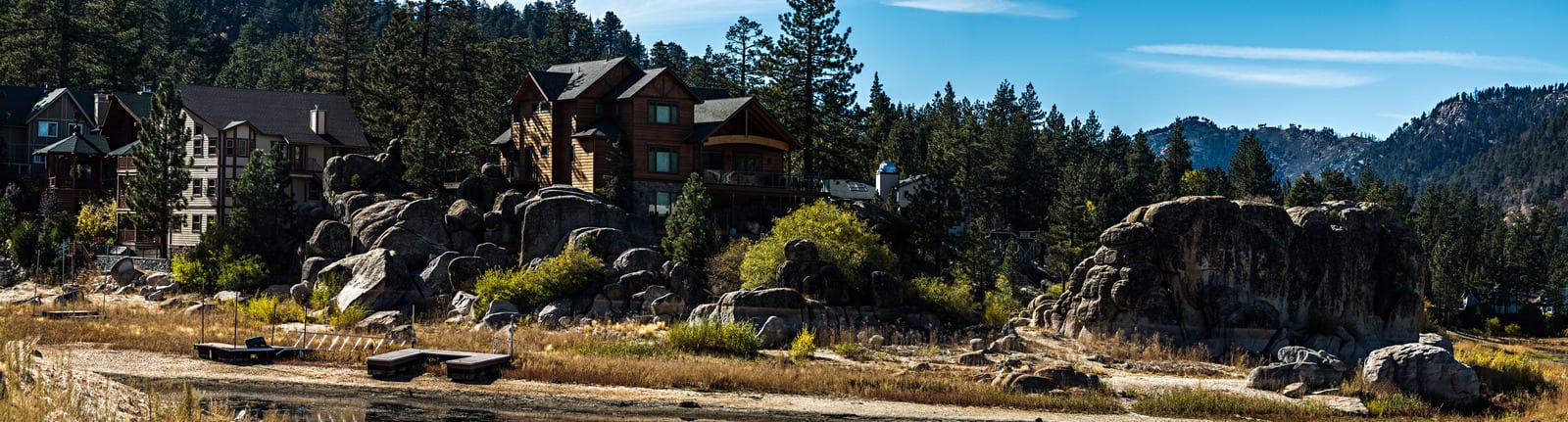 Big Bear Lake cabins nestled among rocky formations and pine trees, showcasing unique wood architecture and mountain scenery under a clear blue sky, ideal for nature enthusiasts and travelers. | Houfy — Book Direct