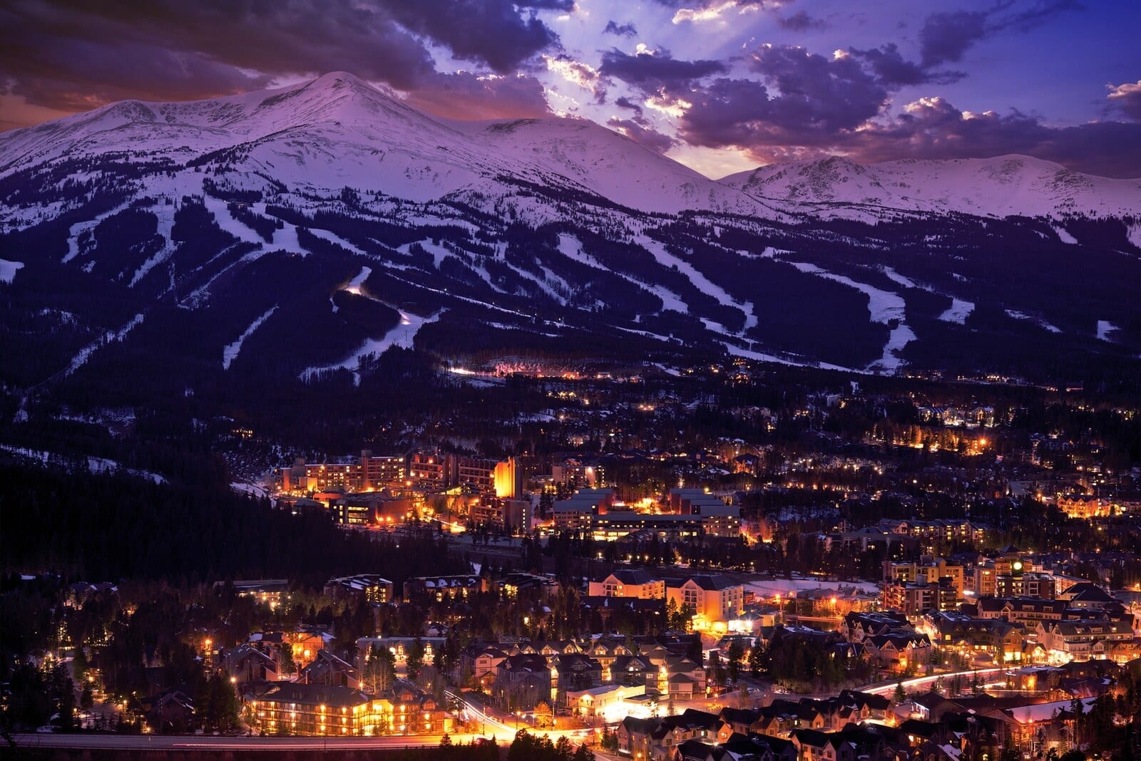 Breckenridge lights up beneath snow-covered mountains at dusk, showcasing winding ski trails and cozy alpine architecture, creating a serene winter wonderland perfect for ski enthusiasts. | Houfy — No Fees, Book Direct