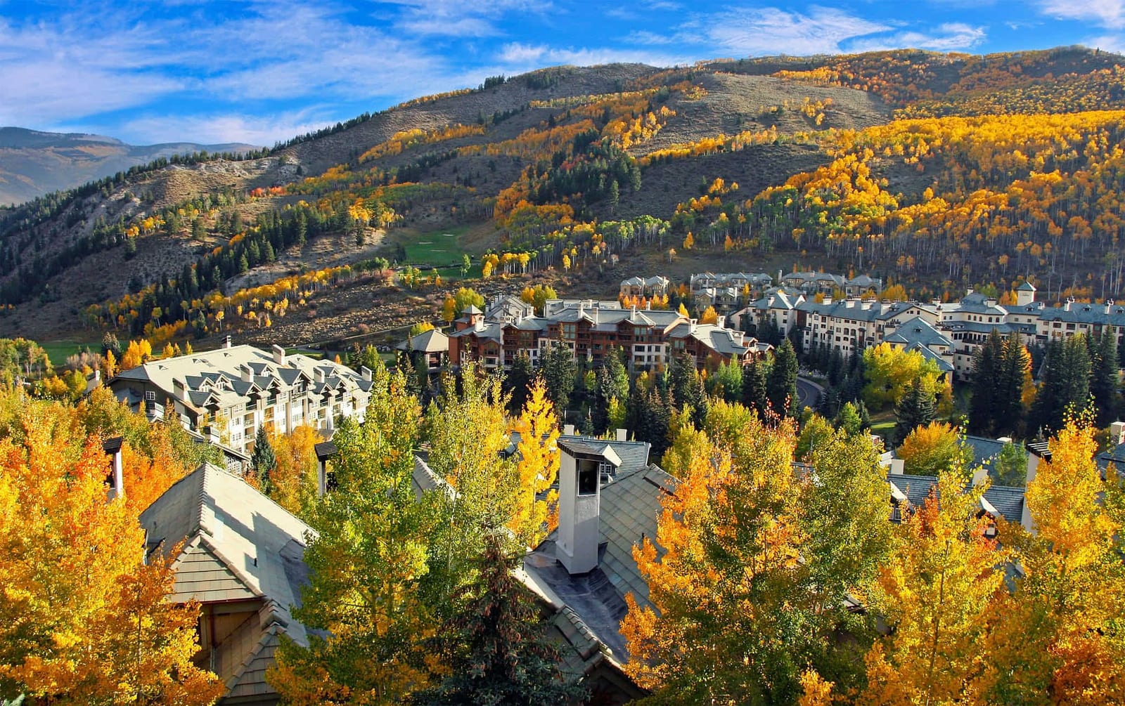 Aerial view of Beaver Creek, Colorado luxury mountain resort lodges nestled among glowing golden aspen trees and deep evergreen forests during peak fall foliage under a crisp blue Rocky Mountain sky — book a fee-free Beaver Creek vacation rental on Houfy | Houfy — No Fees, Book Direct