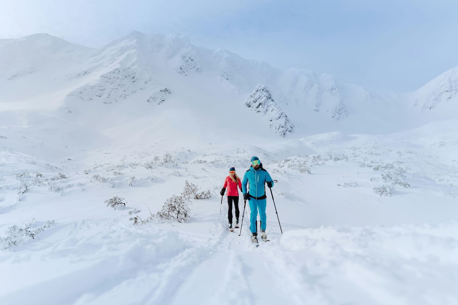 A couple cross-country skiing through a vast snow-covered mountain wilderness — book a fee-free cross-country ski vacation rental on Houfy. | Houfy — No Fees, Book Direct