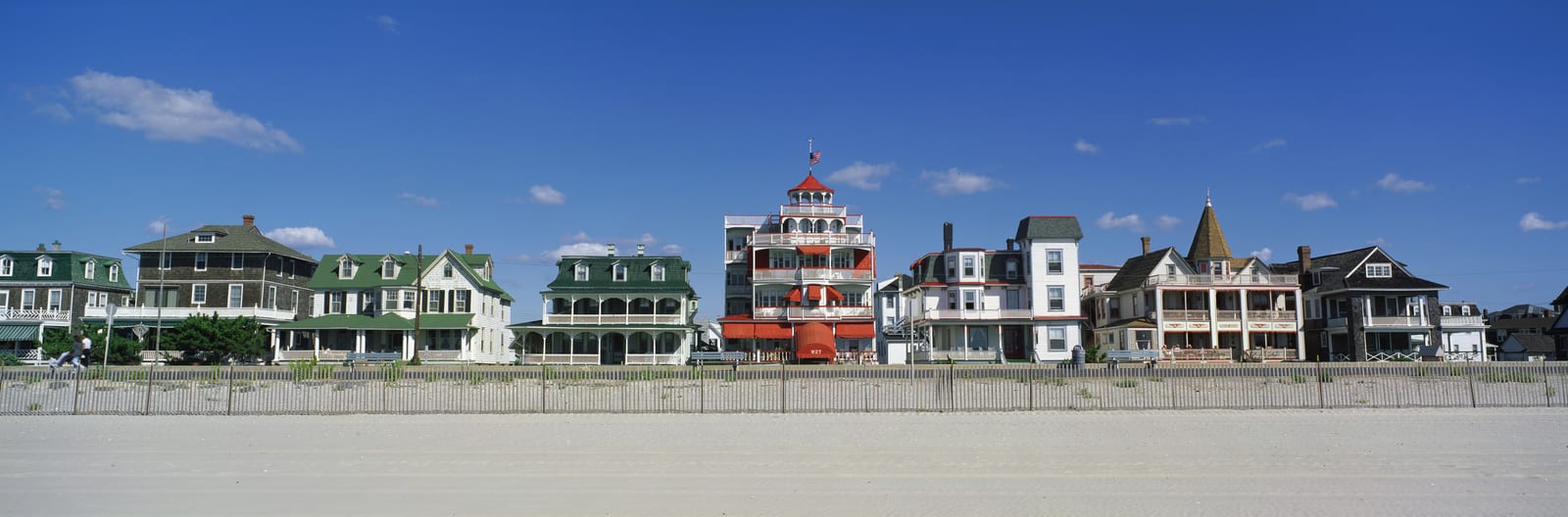 Victorian-era beachfront houses with vibrant architecture under a clear blue sky in Cape May, New Jersey. Highlighting a unique lighthouse-shaped building amidst the colorful historic homes. | Houfy — No Fees, Book Direct