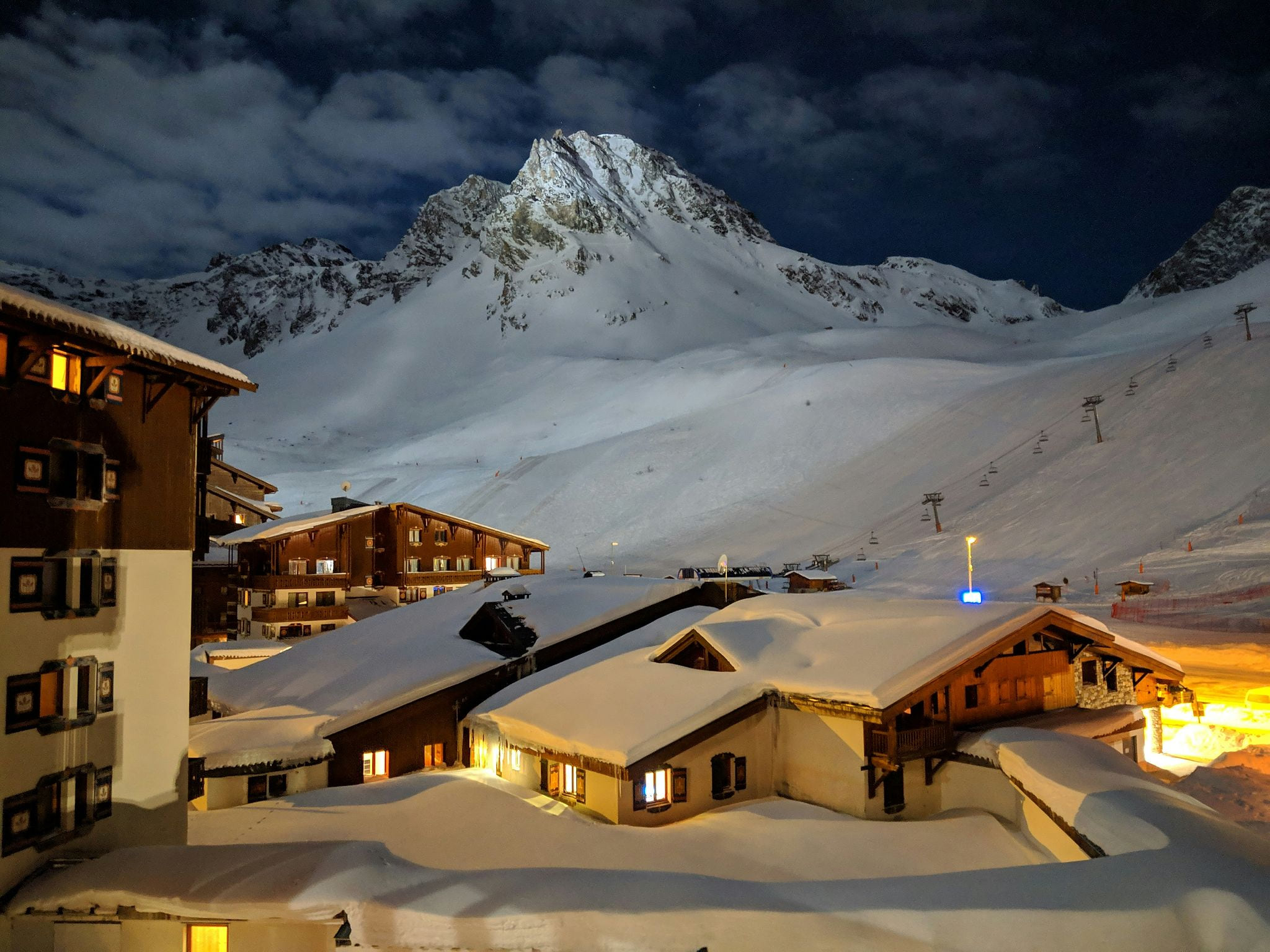 Cozy ski-in ski-out vacation rental chalets in Tignes, French Alps at night — heavy snow rooftops, glowing amber windows, and mountain views — book direct on Houfy | Houfy — No Fees, Book Direct