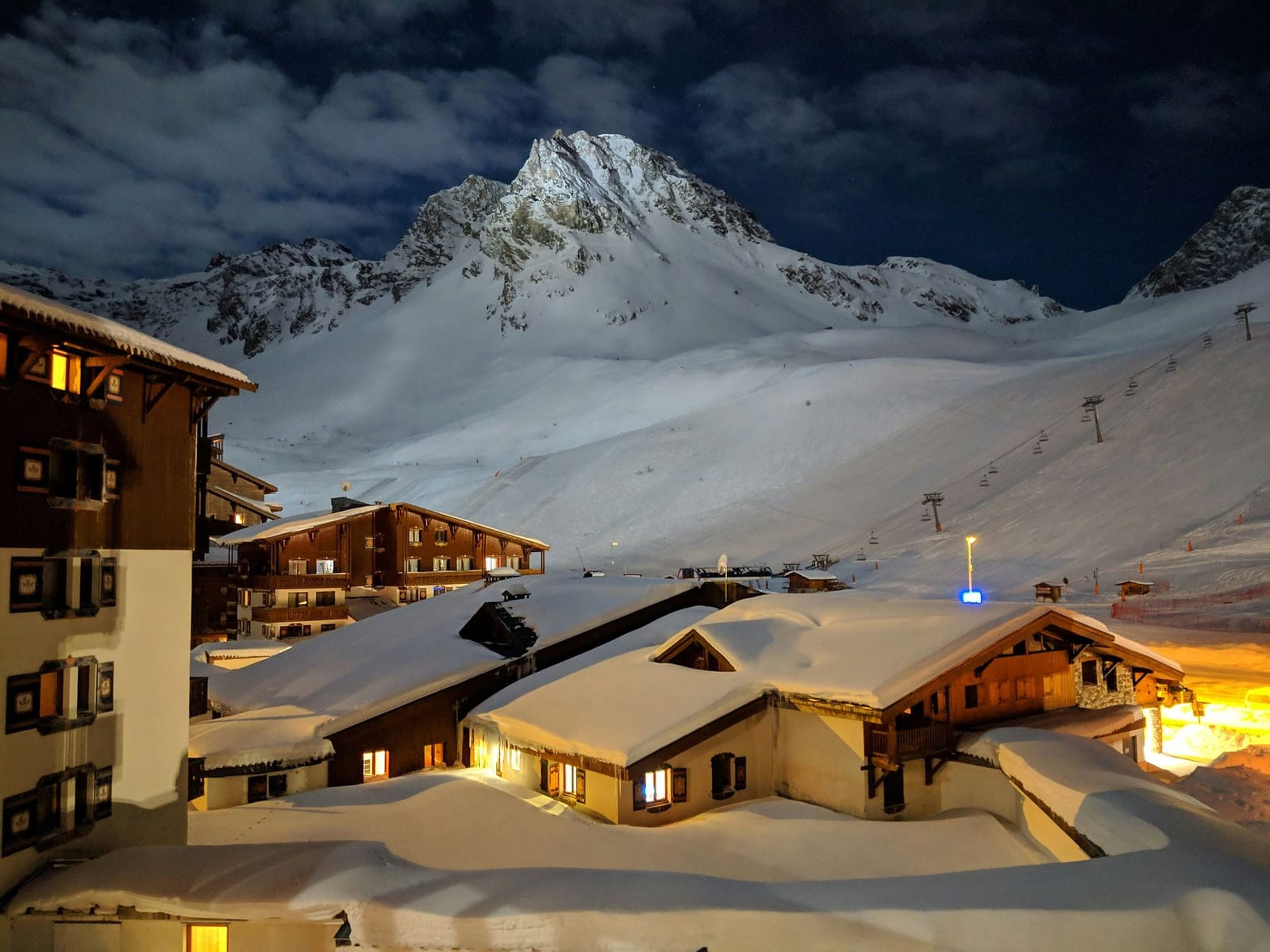 Cozy ski-in ski-out vacation rental chalets in Tignes, French Alps at night — heavy snow rooftops, glowing amber windows, and mountain views — book direct on Houfy | Houfy — No Fees, Book Direct