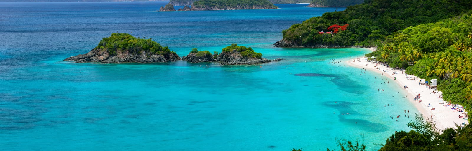Turquoise waters and lush green islands characterize the picturesque landscape of Trunk Bay, Saint John, with a white sandy beach and scattered swimmers adding a lively touch to this tropical paradise. | Houfy — No Fees, Book Direct