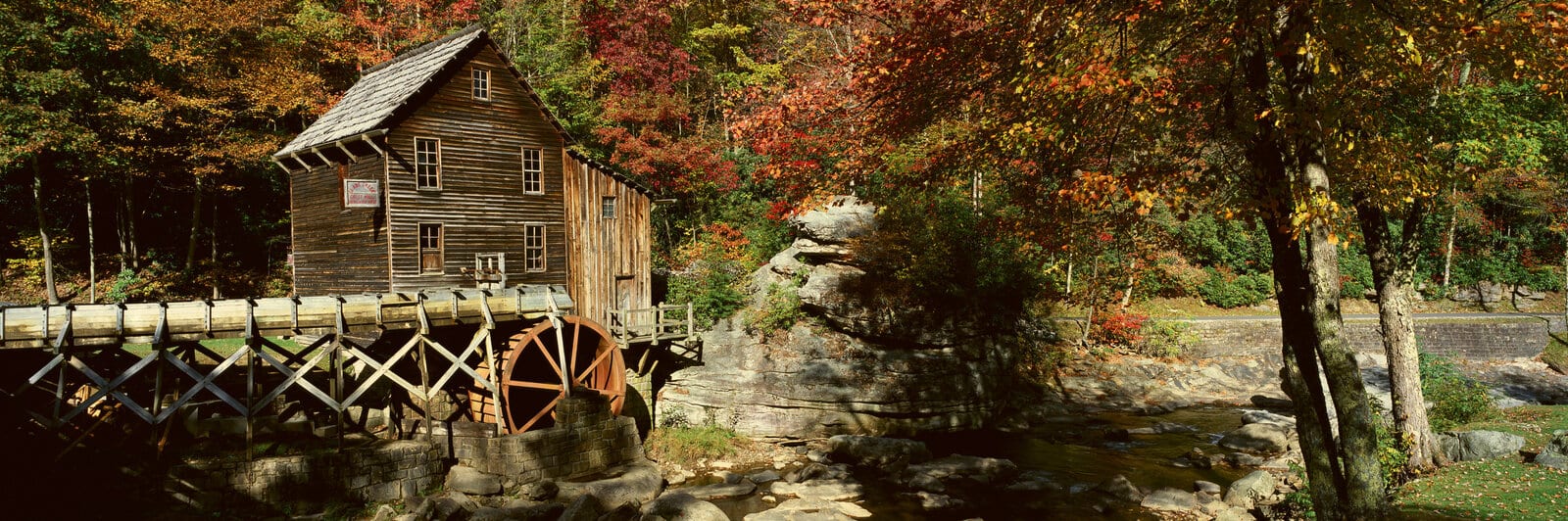 Historic wooden grist mill with a waterwheel nestled among vibrant autumn foliage by a rocky stream in Babcock State Park, West Virginia, capturing the quintessential rustic charm of the Appalachian landscape. | Houfy — No Fees, Book Direct