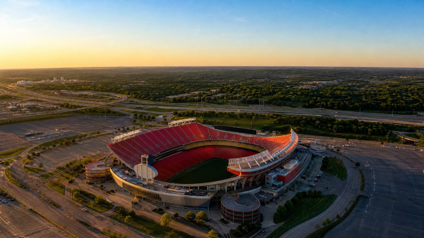 Aerial view of Arrowhead Stadium in Kansas City at sunset showing the iconic red seating bowl surrounded by vast parking lots and highways