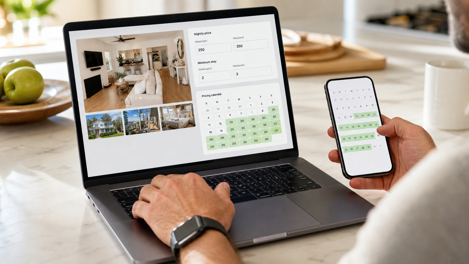 Host updating vacation rental pricing and calendar on a laptop and phone at a kitchen island.