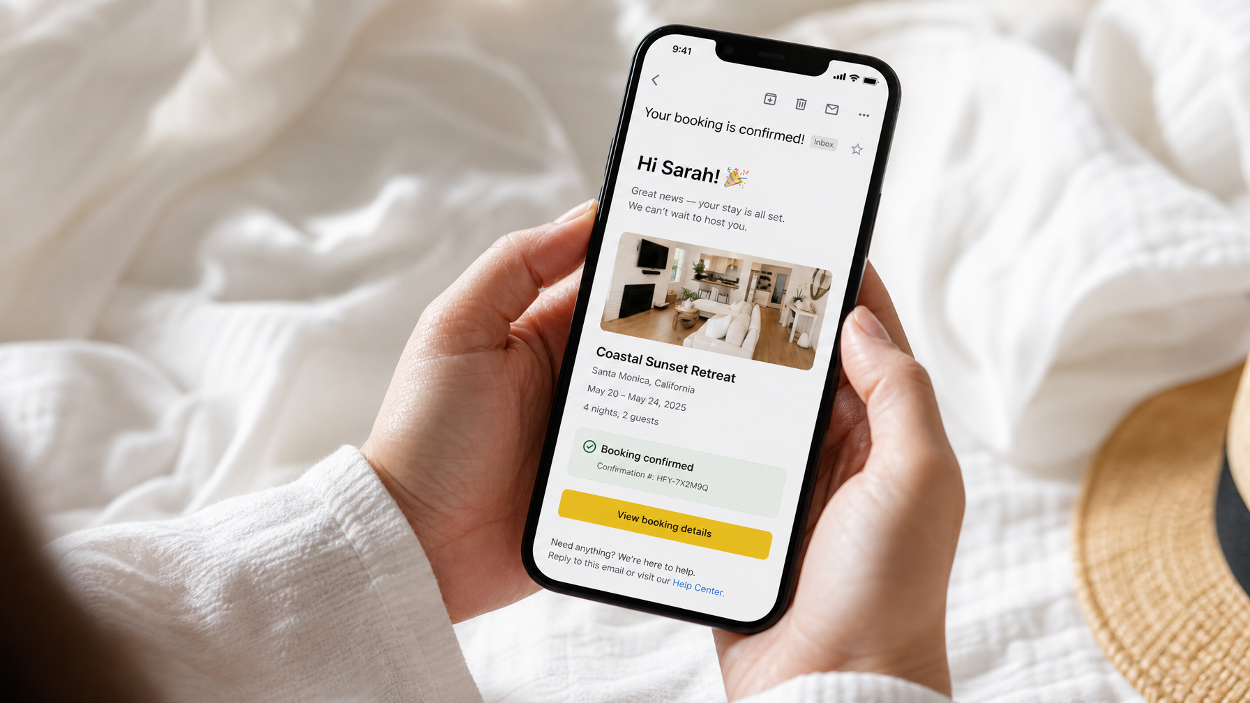 A guest holding a phone that shows a vacation rental booking confirmation email with the property name, dates, and a confirmed status