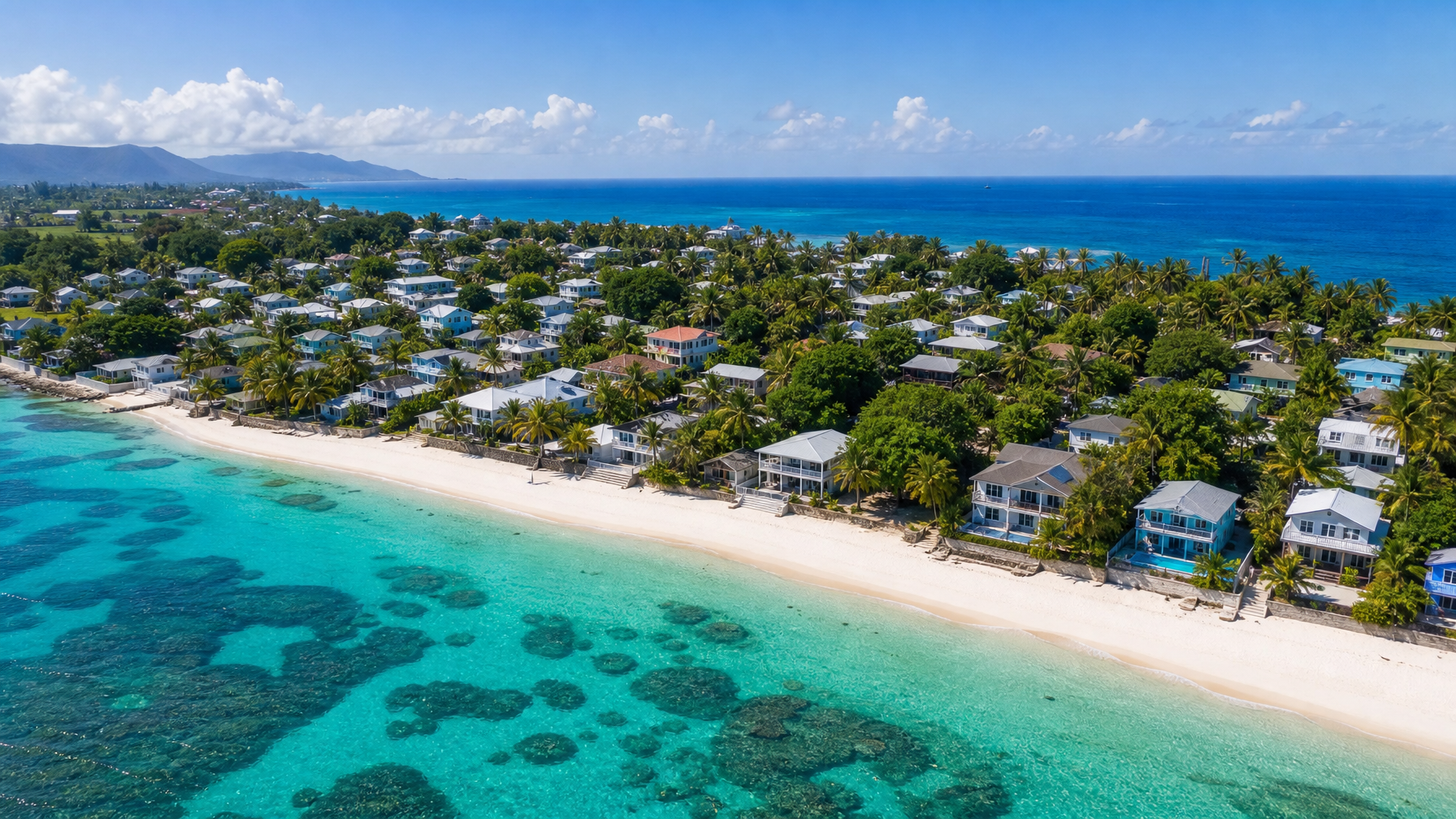 Aerial drone view of colorful beachfront vacation rental villas along a white sand beach and coral reef, bookable fee-free on Houfy