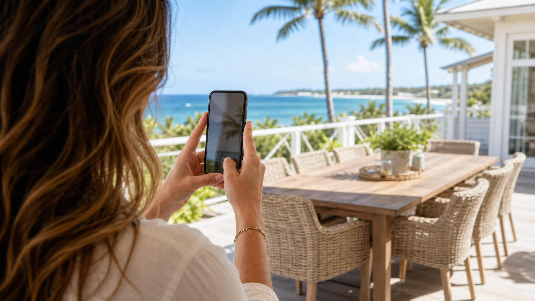 Host hands filming a sunlit vacation rental terrace on a smartphone for Instagram Reels