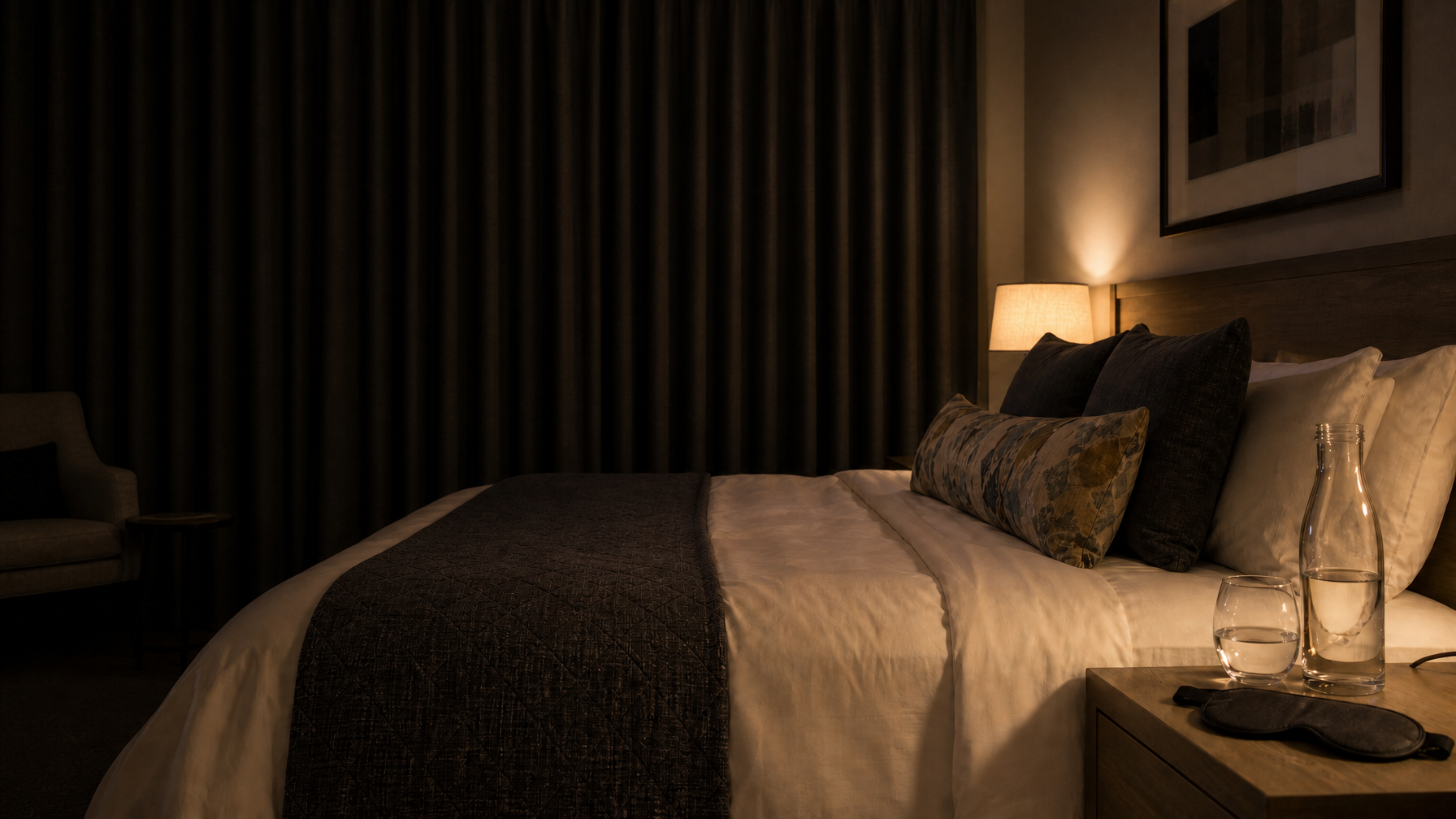Sleep-ready vacation rental bedroom with blackout curtains closed, eye mask, and water carafe by soft lamp light