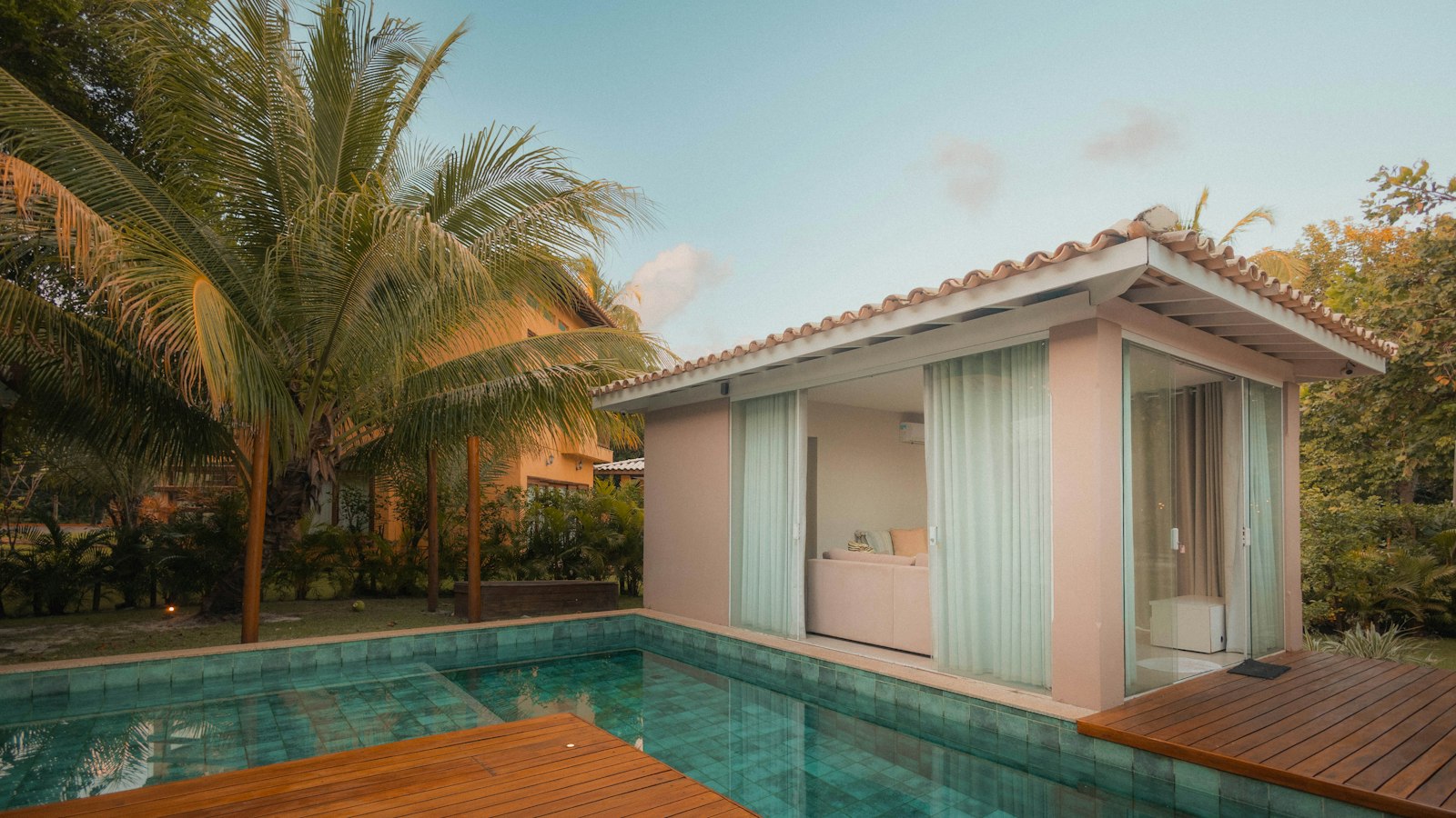 Poolside cabana and loungers beside a turquoise pool, framed by tall palms.