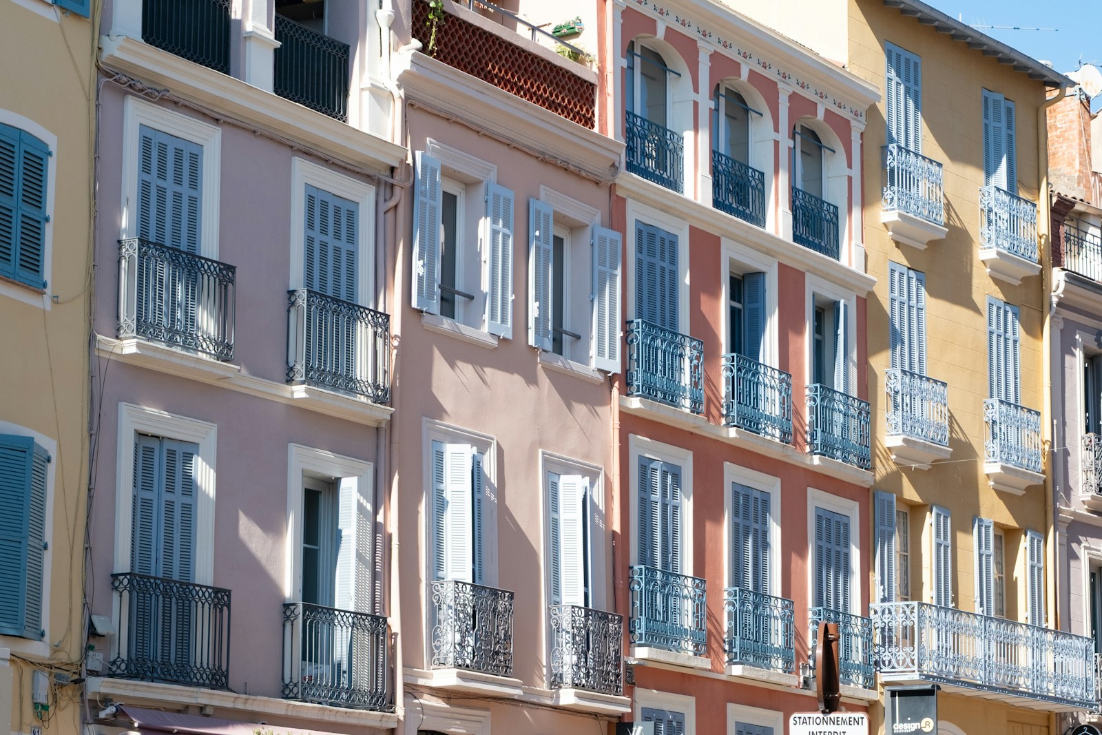 A row of pastel-painted townhouses with wrought-iron balconies and shutters in a French town