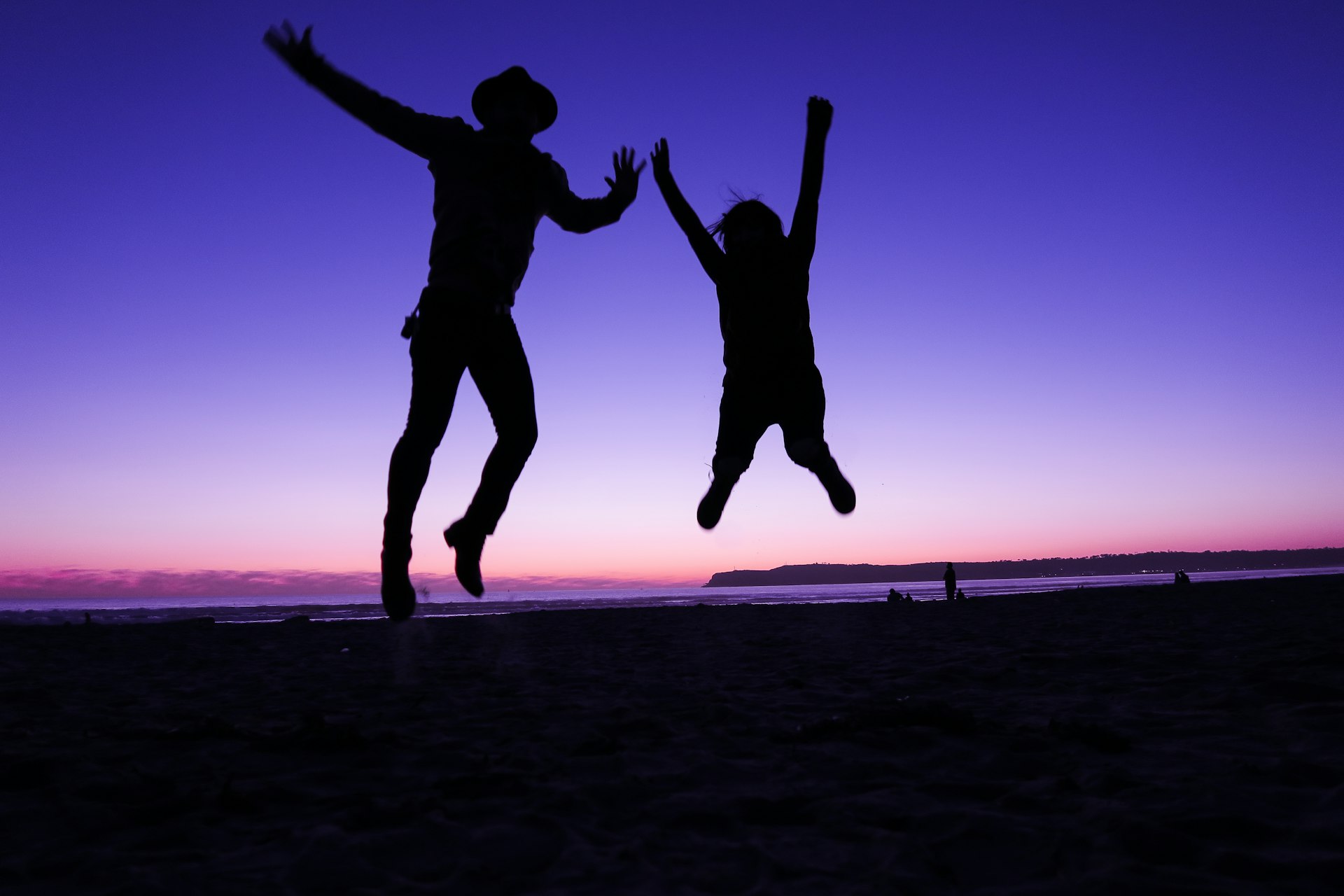 Two people jumping on Coronado Beach at sunset near Hotel del Coronado