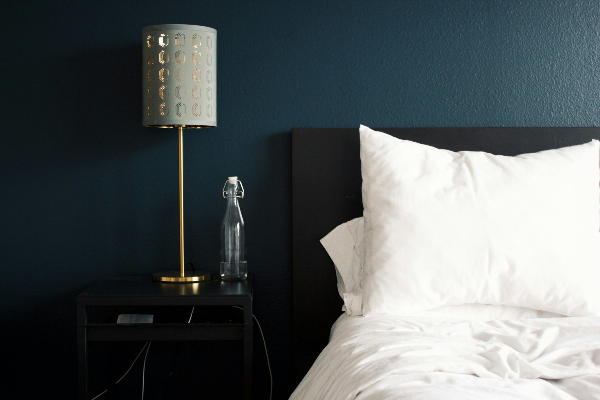 A bed made up with white linens beside a lamp on a nightstand