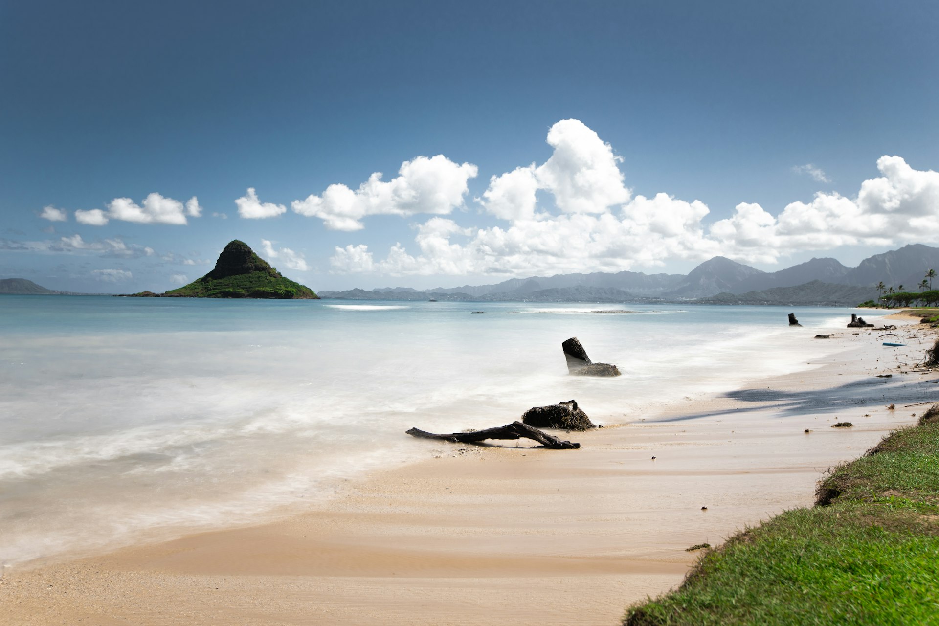 Calm turquoise water and sandy shoreline with green hills in the distance
