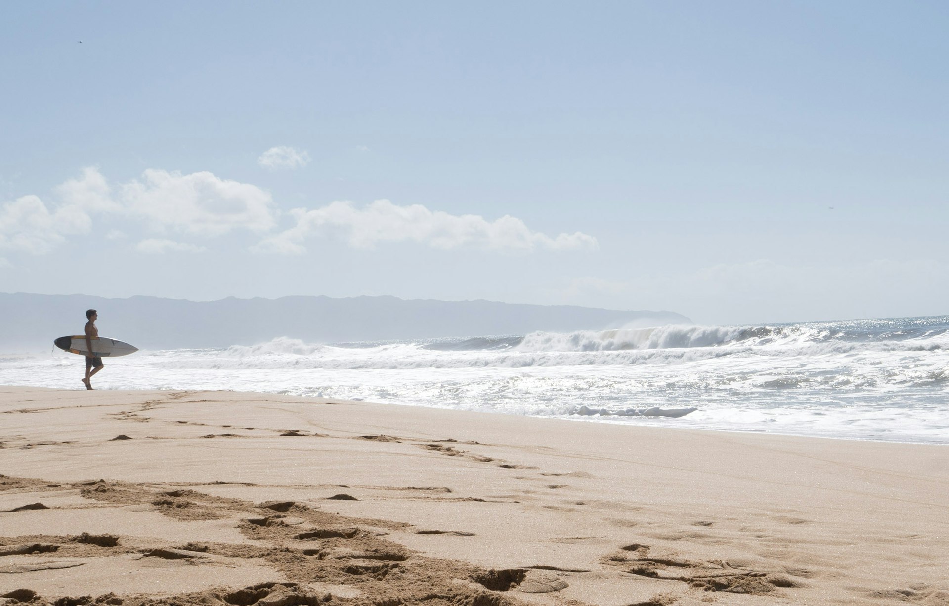 Person holding a white surfboard standing on the seashore in daylight