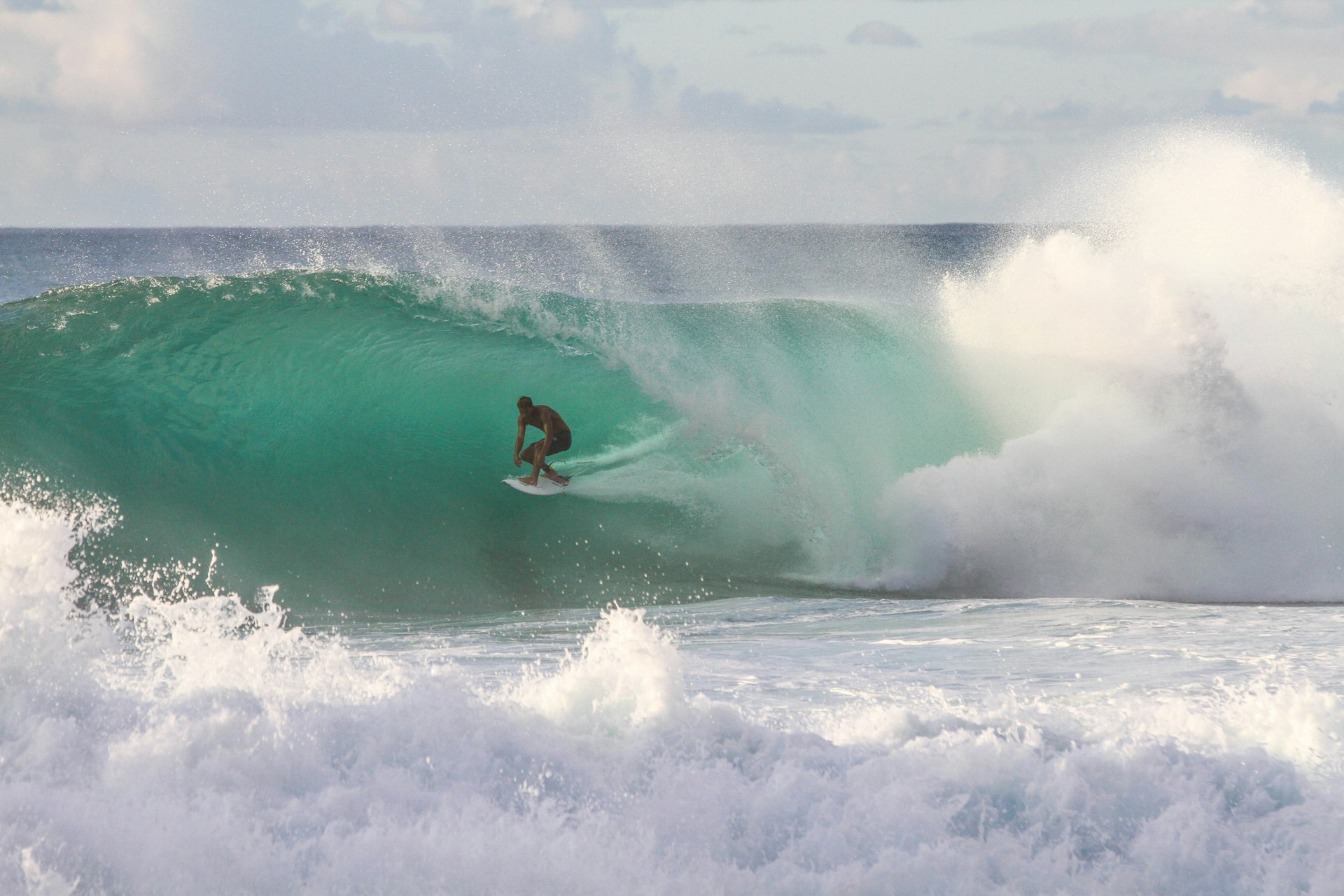 Surfer riding under a large green ocean wave