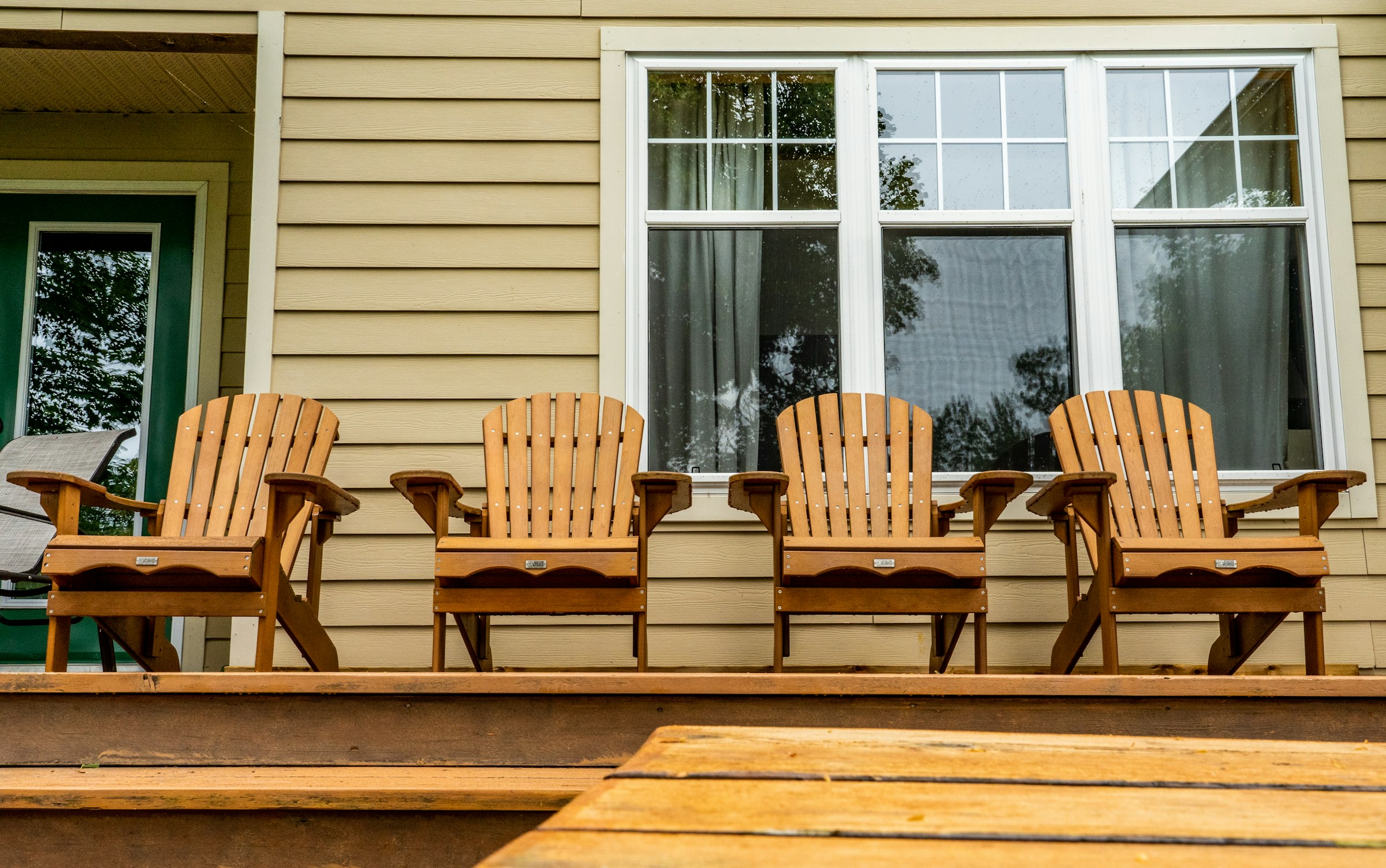Wooden Muskoka chairs and a small table on a cottage deck in afternoon sun