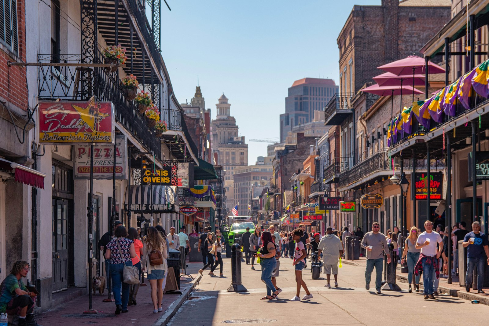 People walking a busy French Quarter street lined with multi-story buildings
