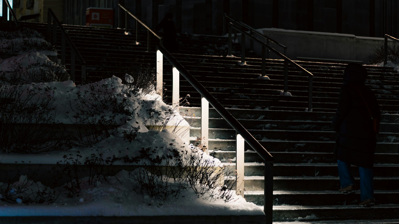 Person walking up snow-covered outdoor stairs at night