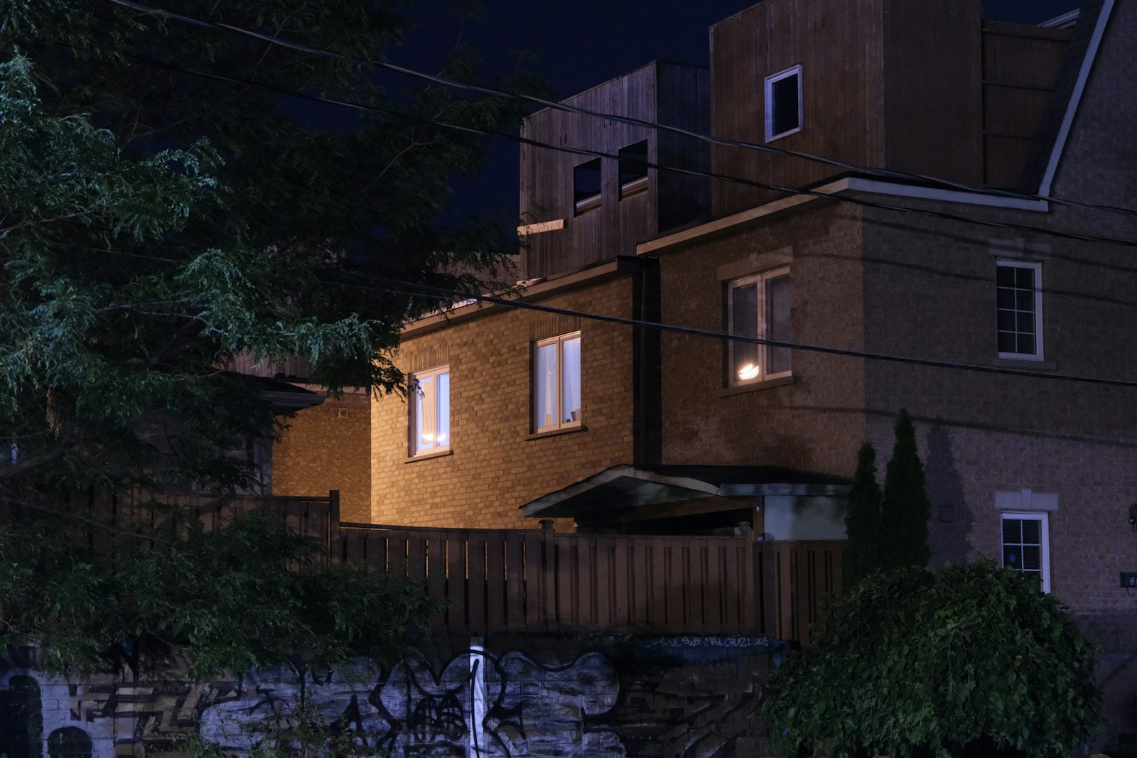 Brick house with glowing windows at night behind a wooden fence