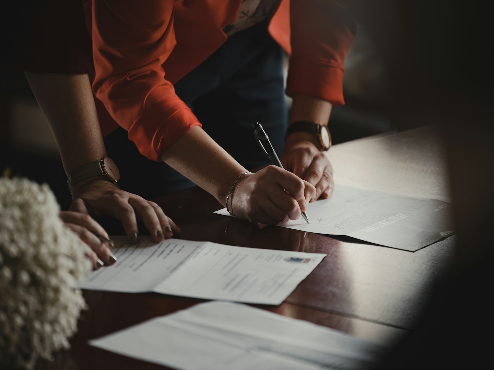 Person in an orange long-sleeve shirt writing notes on white paper at a desk