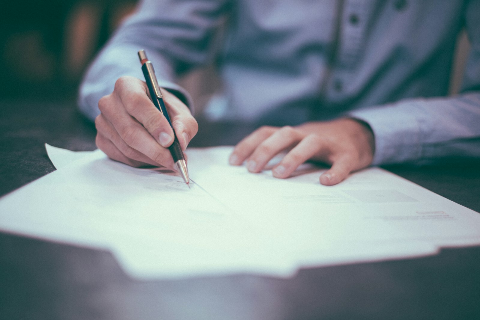 Hands reviewing and signing paper contract documents on a wooden desk