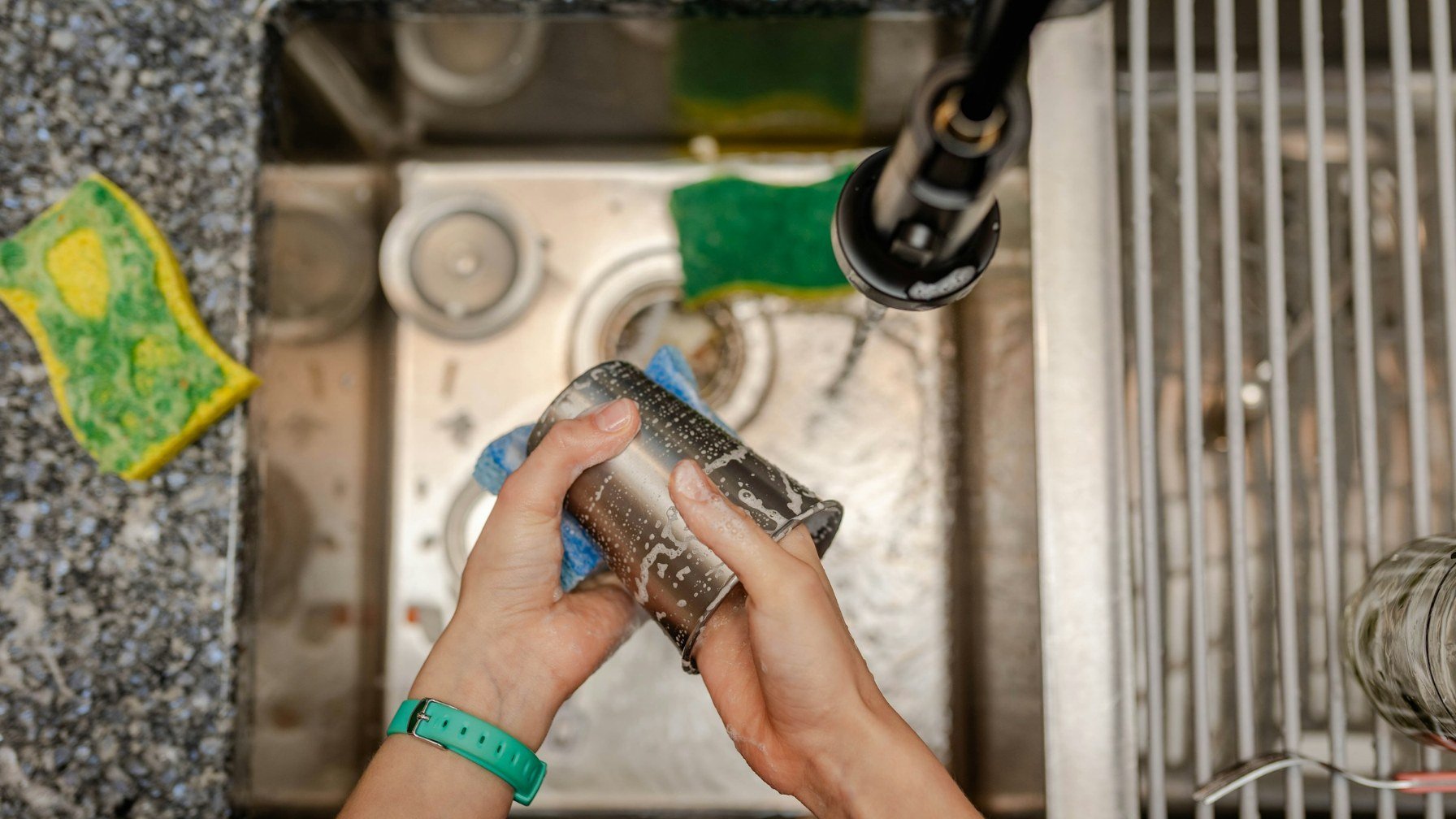 A person washing up at a stainless steel kitchen sink