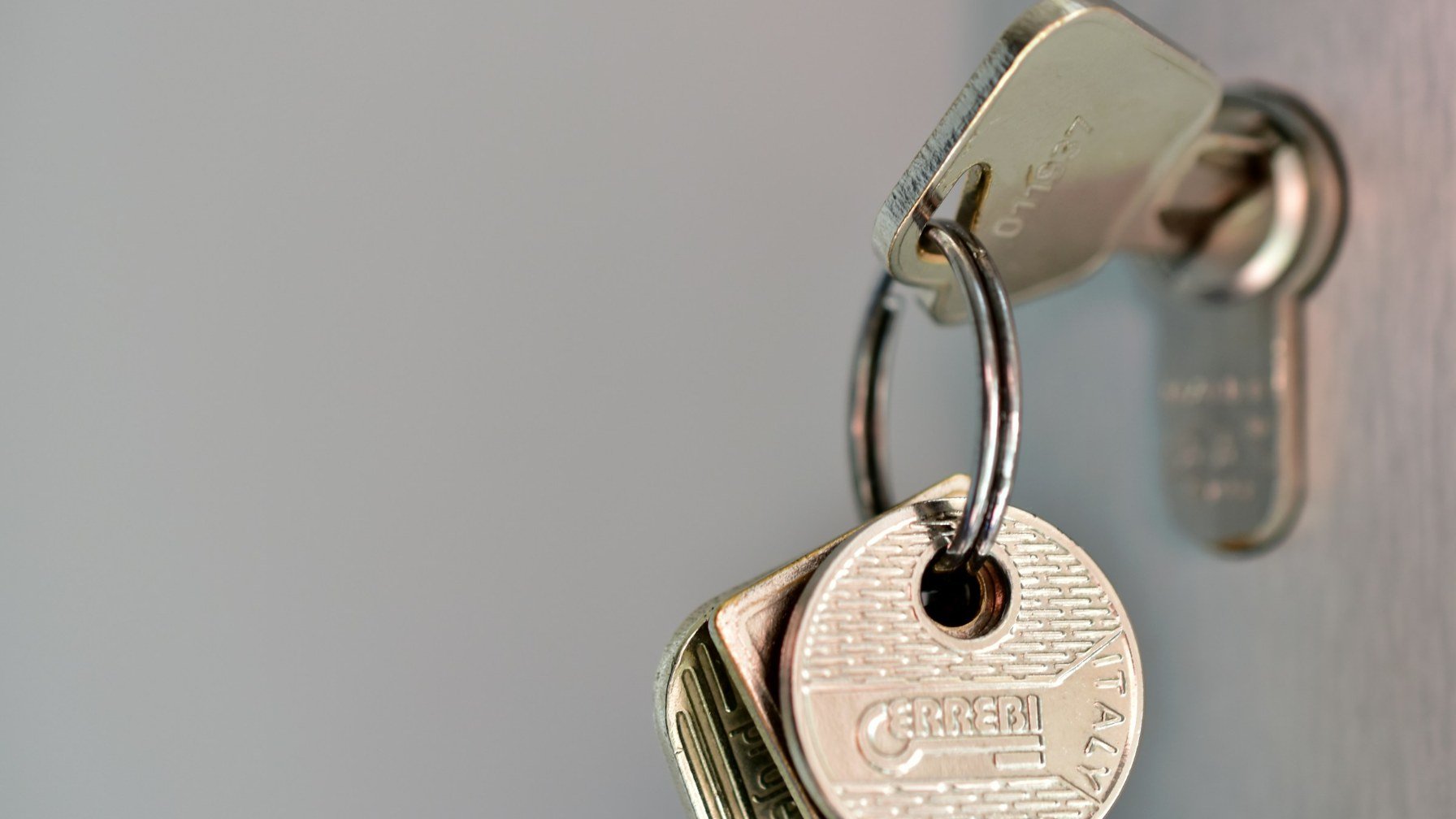 A door key on a ring with a plain round fob, hanging against a pale wall