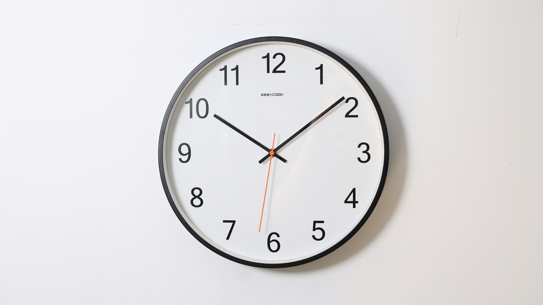A plain round analog wall clock with black hands on a white wall