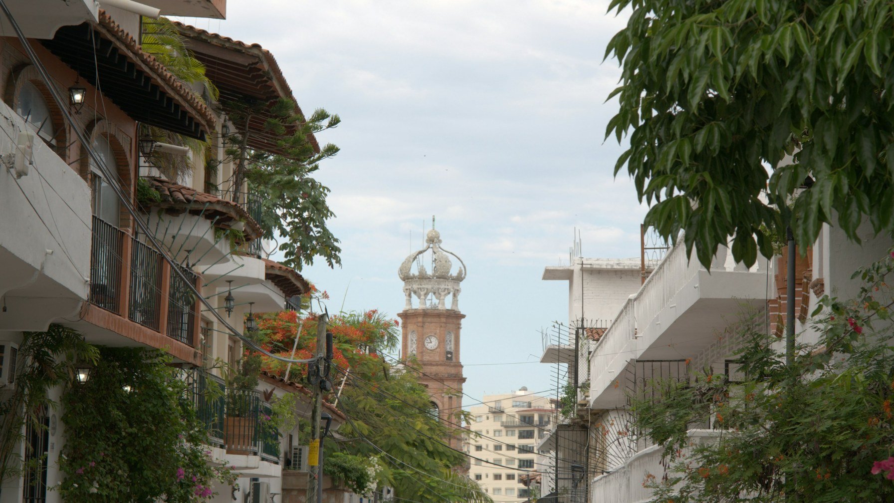 A street in Puerto Vallarta lined with balconied buildings, the crowned tower of the Guadalupe church rising at the end