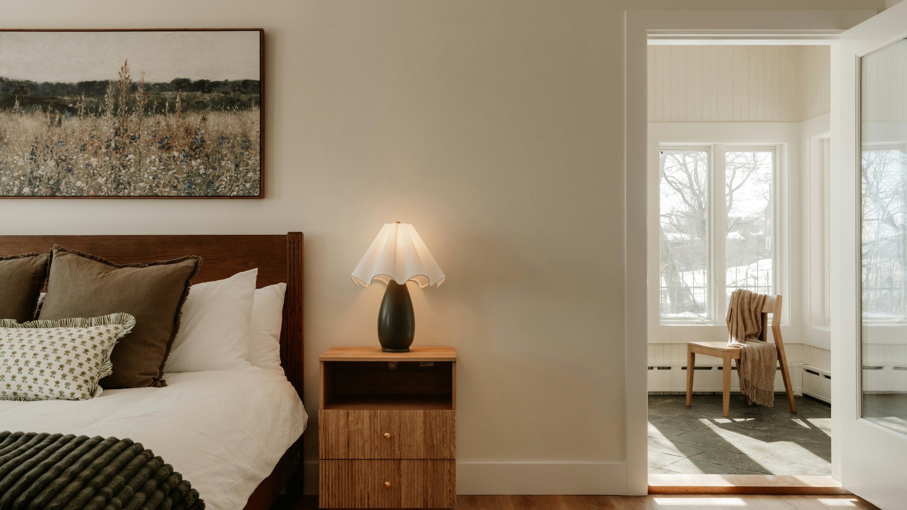 A made bed seen from the bedroom doorway with daylight from a window