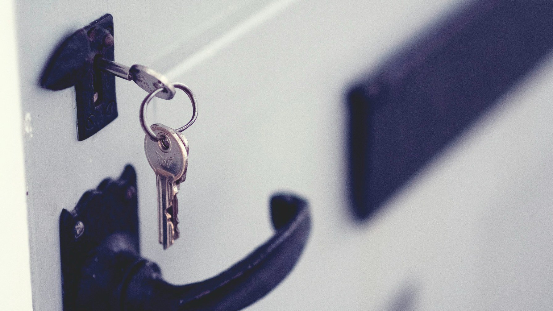 A key hanging on a hook beside the handle of a white front door
