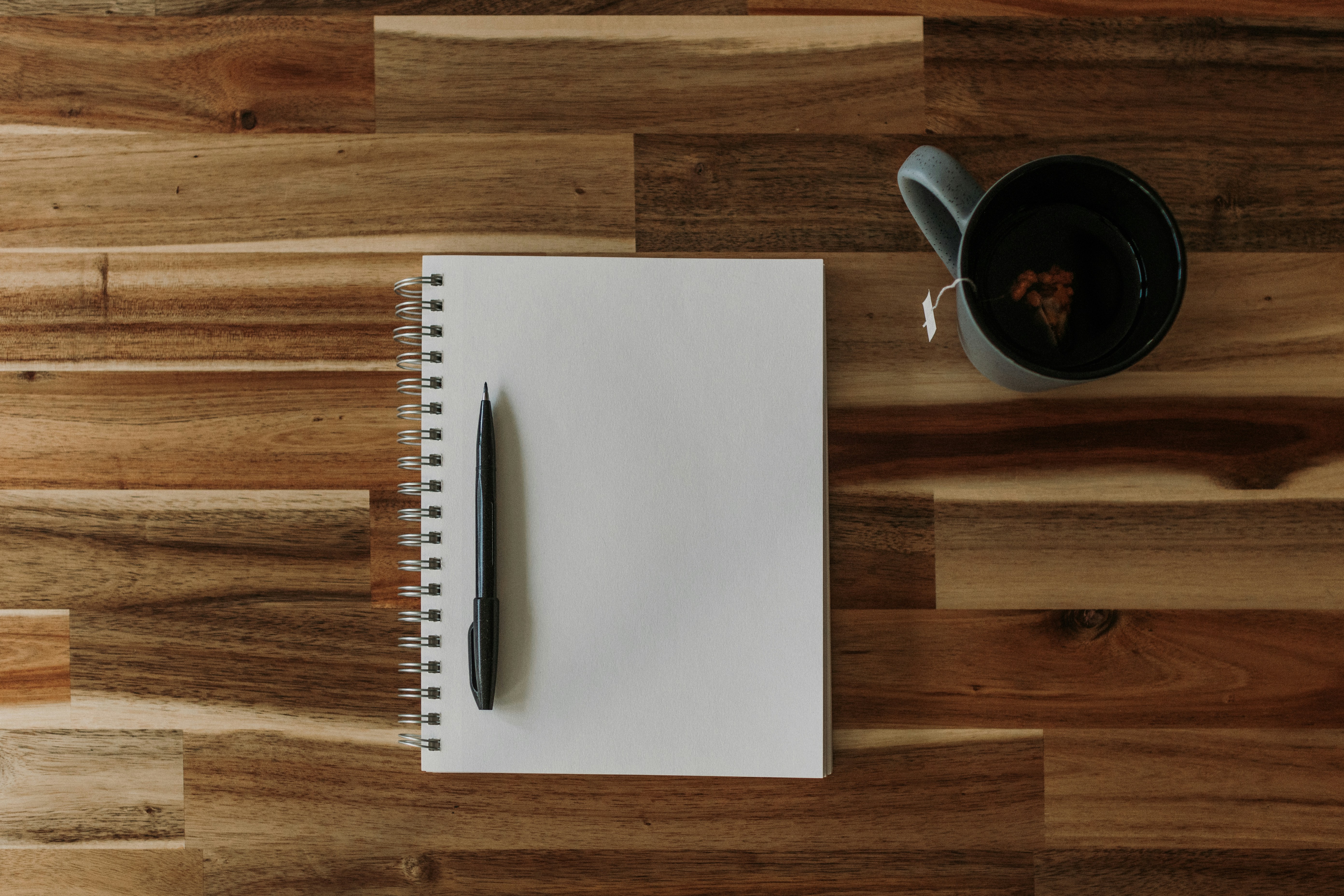 An open notebook, a pen and a cup of coffee on a wooden table