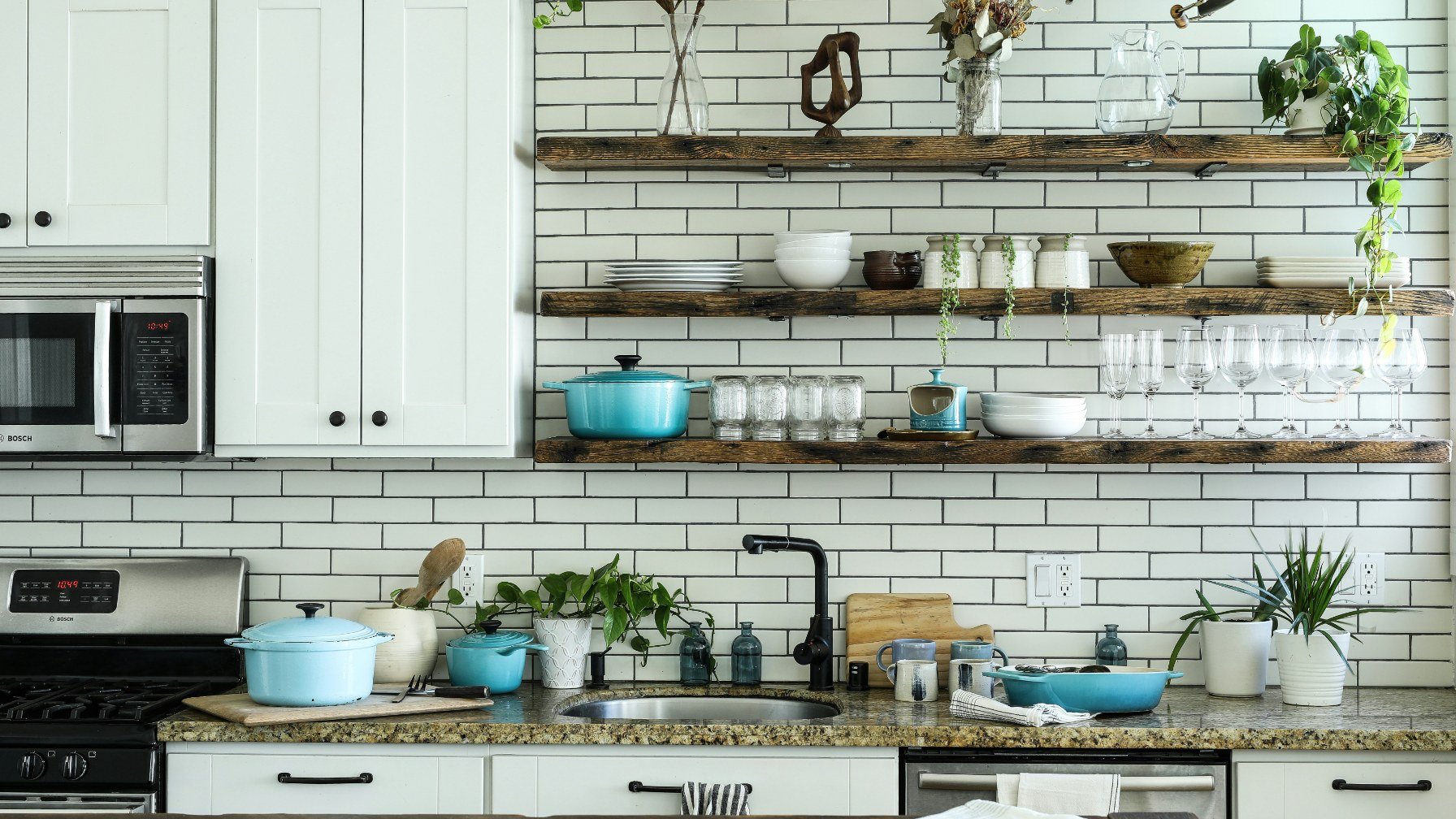 A well-stocked kitchen with open shelves of crockery, pans and a tiled wall