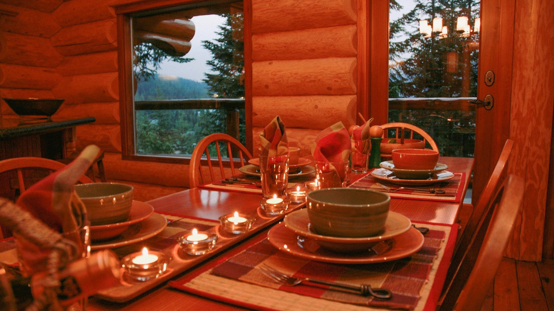 A log cabin dining table laid with plates and lit candles beside a window