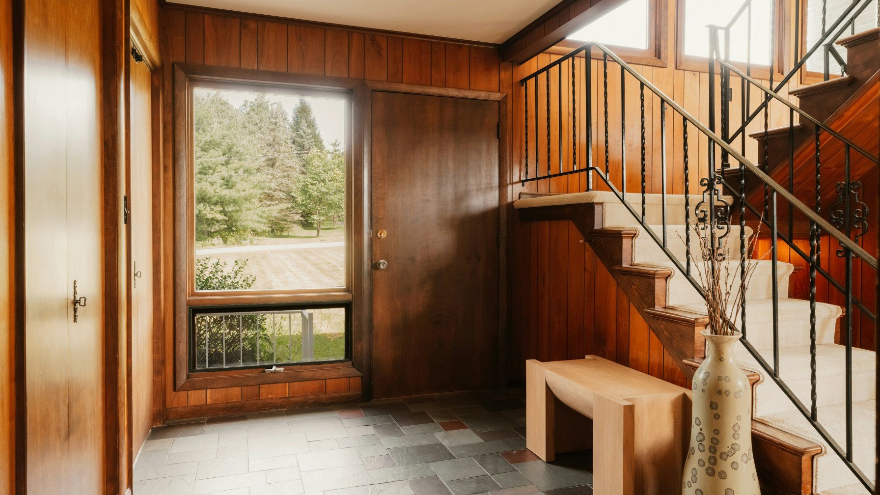 A bright entrance hall with a staircase and daylight coming through a window onto trees