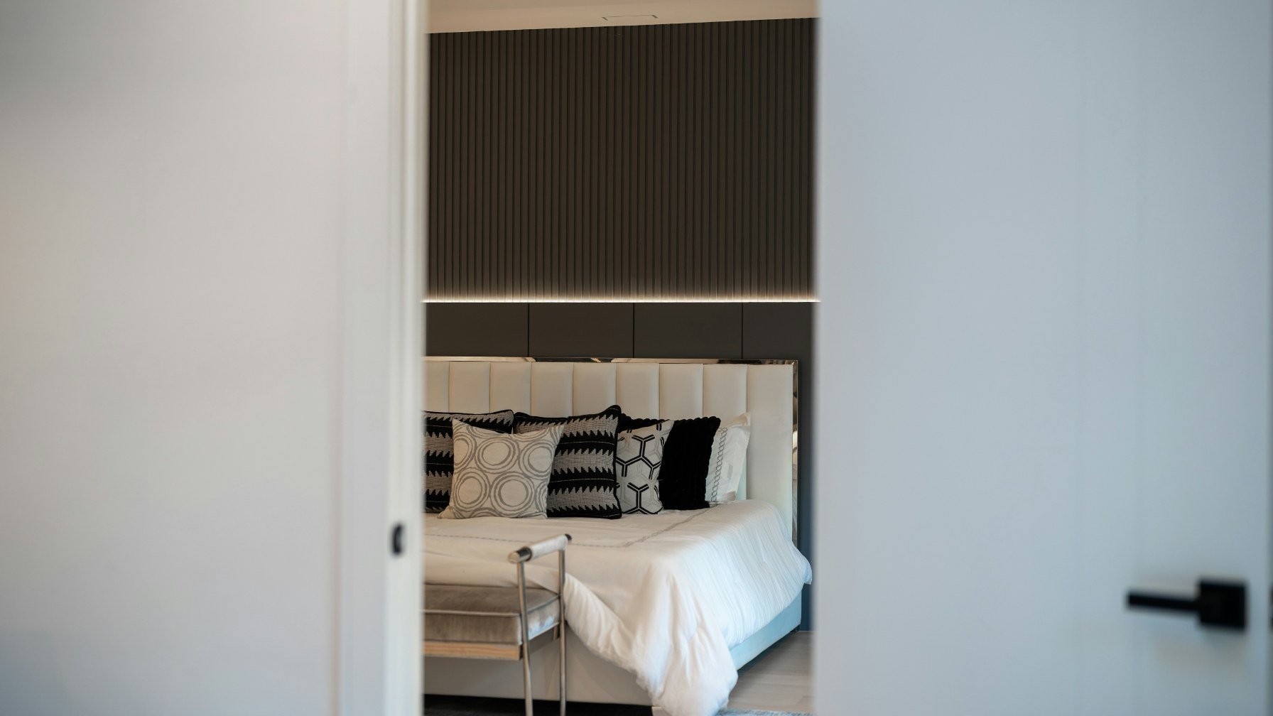 A tidy made bed with white linen seen through an open bedroom doorway