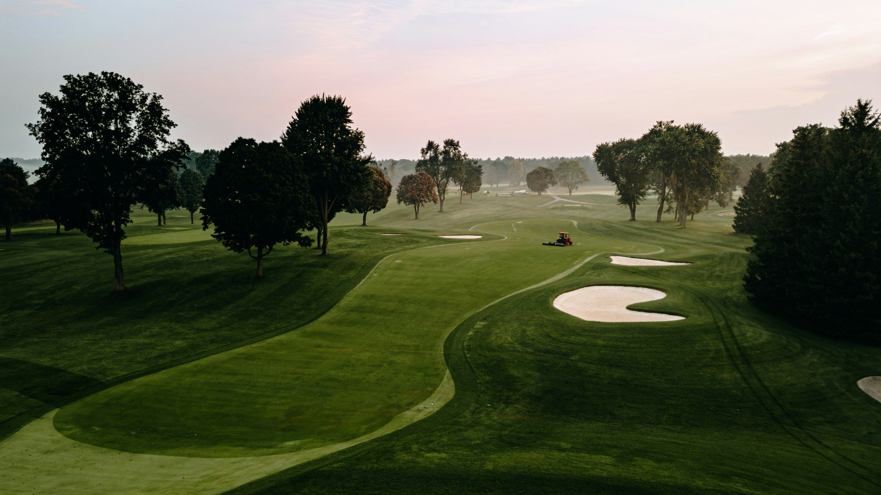 A golf fairway in early morning light with mist over the grass and sand bunkers