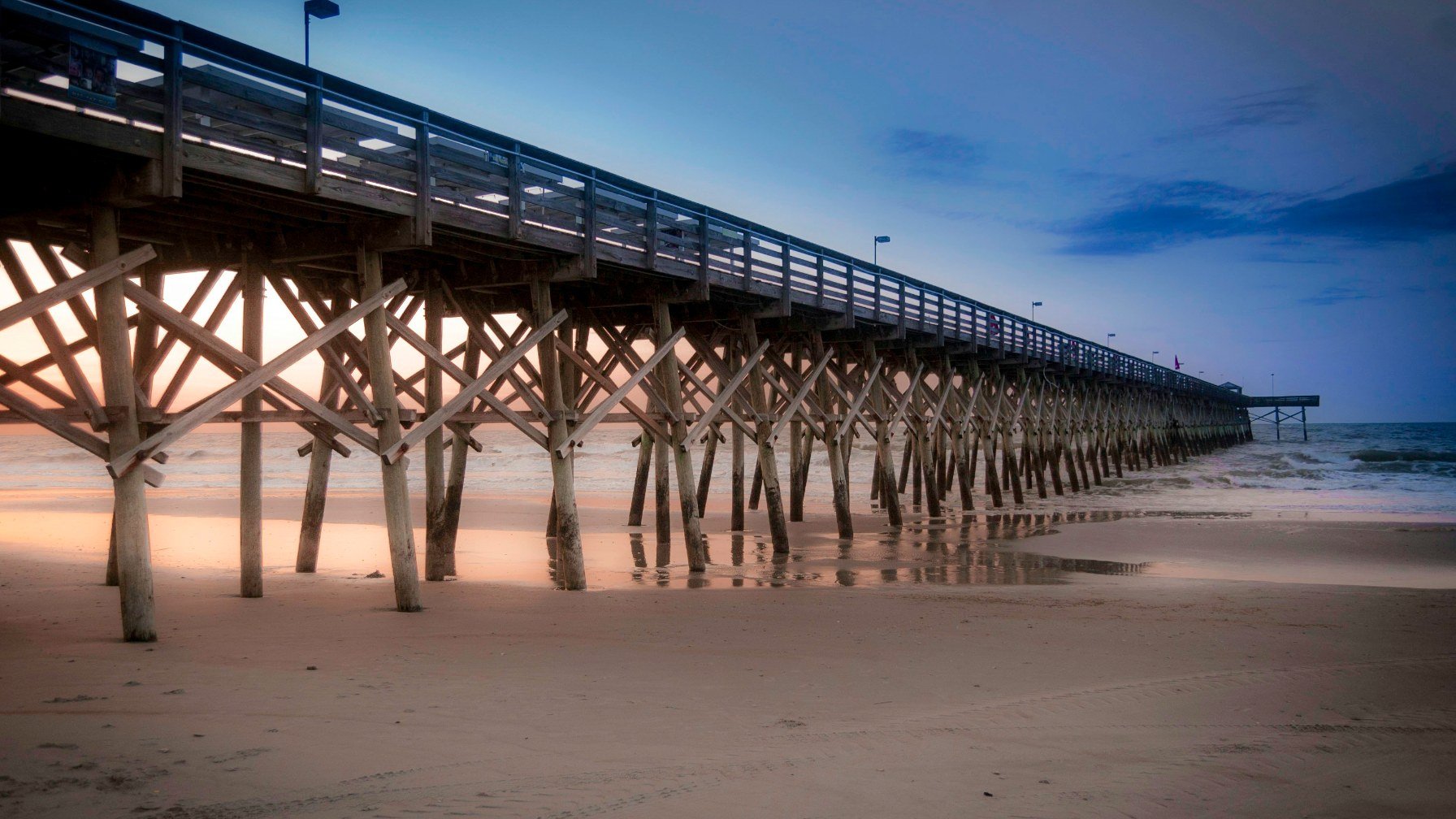 A long wooden pier reaching out over a quiet Myrtle Beach shoreline at first light