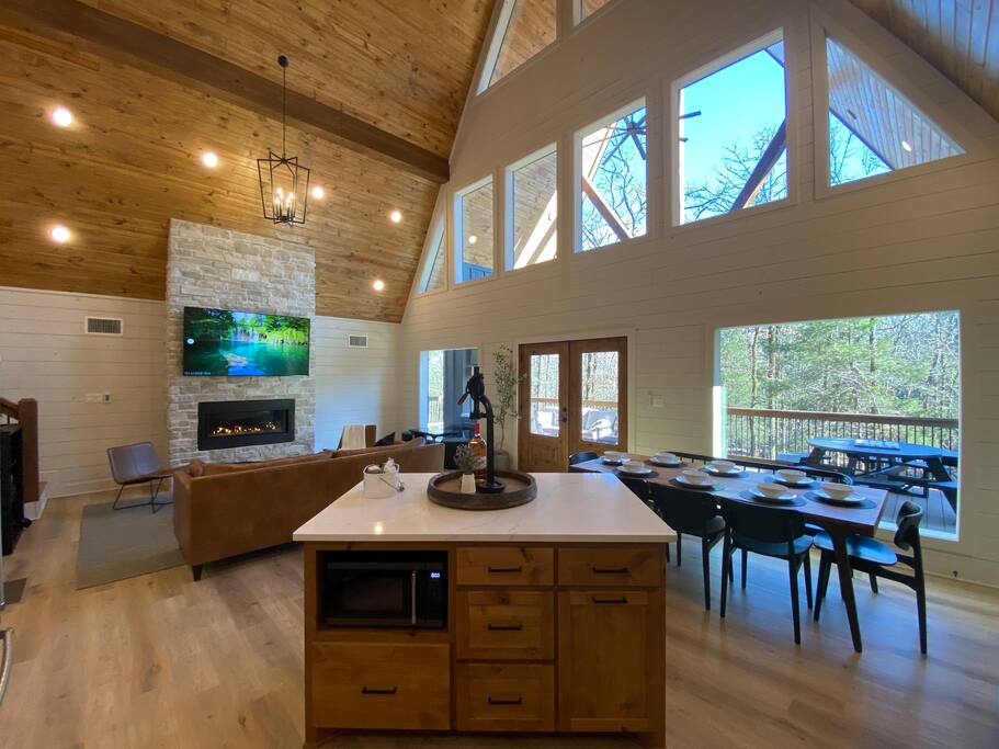 Cozy cabin living room with fireplace, large windows, and modern dining area.