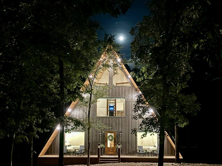 Restful Yay frame cabin glowing at dusk, surrounded by towering trees.