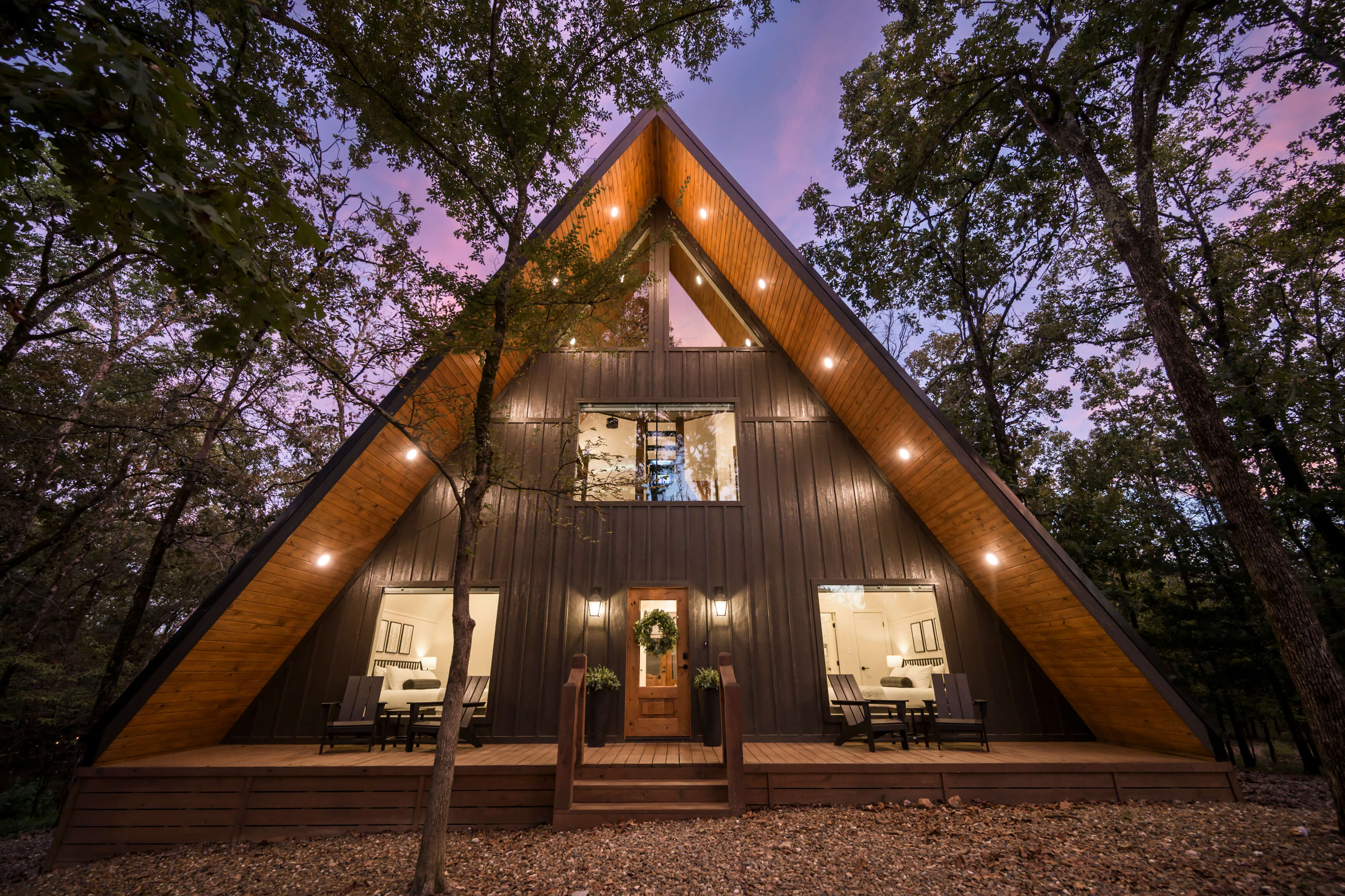 Restful Yay frame cabin glowing at dusk, surrounded by towering trees.