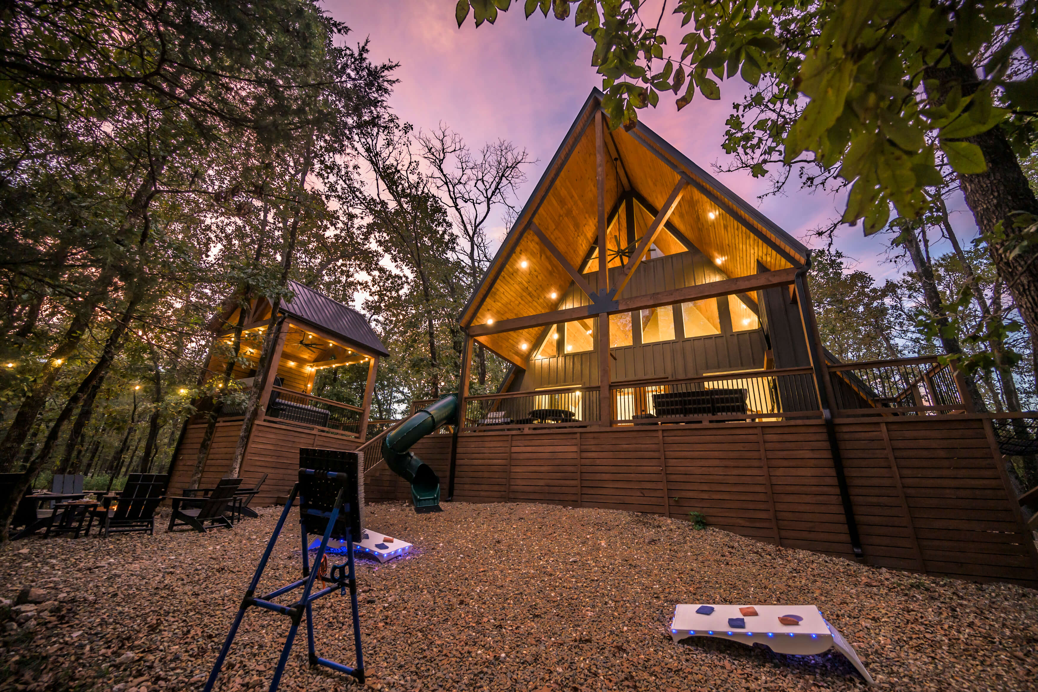 Elevated wooden cabin with playground slide and serene sunset forest view.