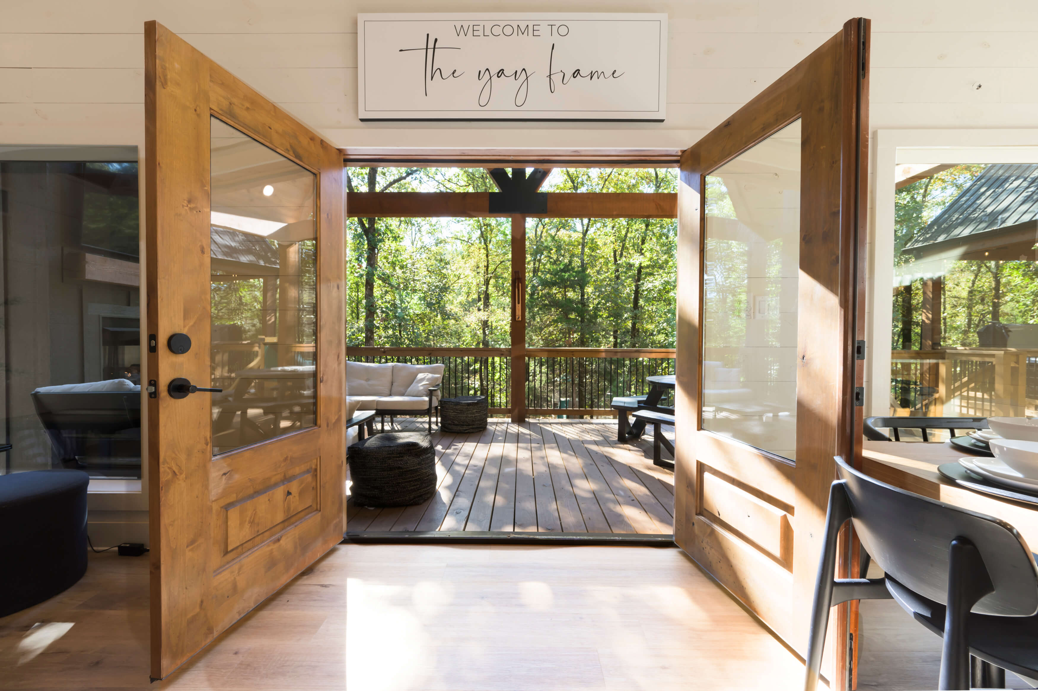 Cozy cabin door opens to a peaceful deck surrounded by lush greenery.