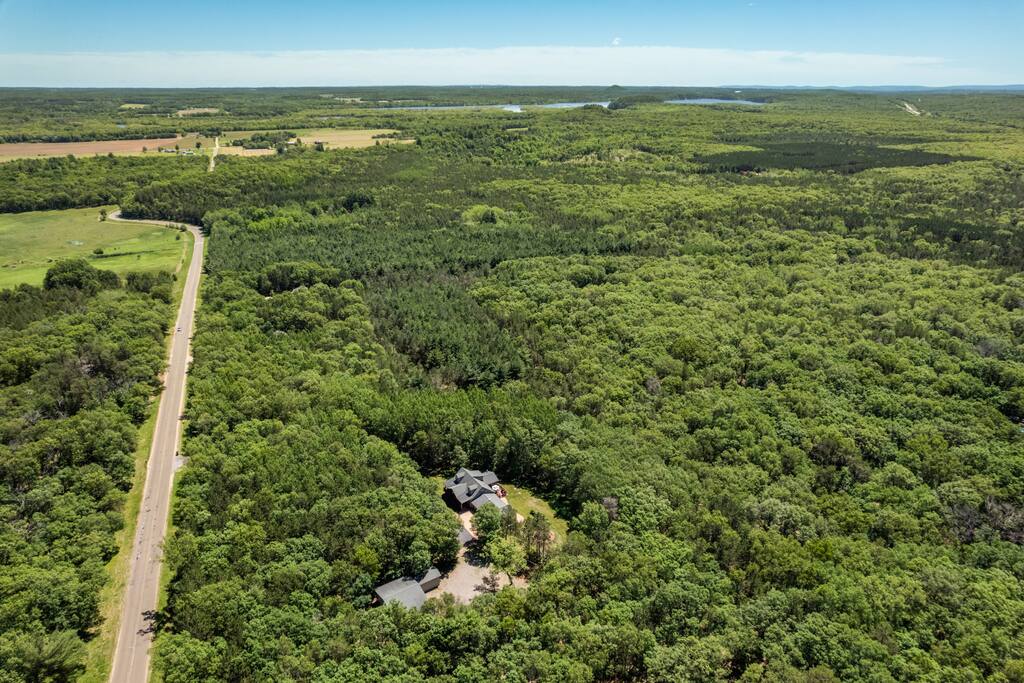 Exterior of the home from drone view with Wisconsin River in the background. This home features 6 acres including trails, firepit, gas and charcoal grills, porch, and deck. Exterior of the home from drone view with Wisconsin River in the background. This home features 6 acres including trails, firepit, gas and charcoal grills, porch, and deck. - Bear Cove Escape - Lyndon Station