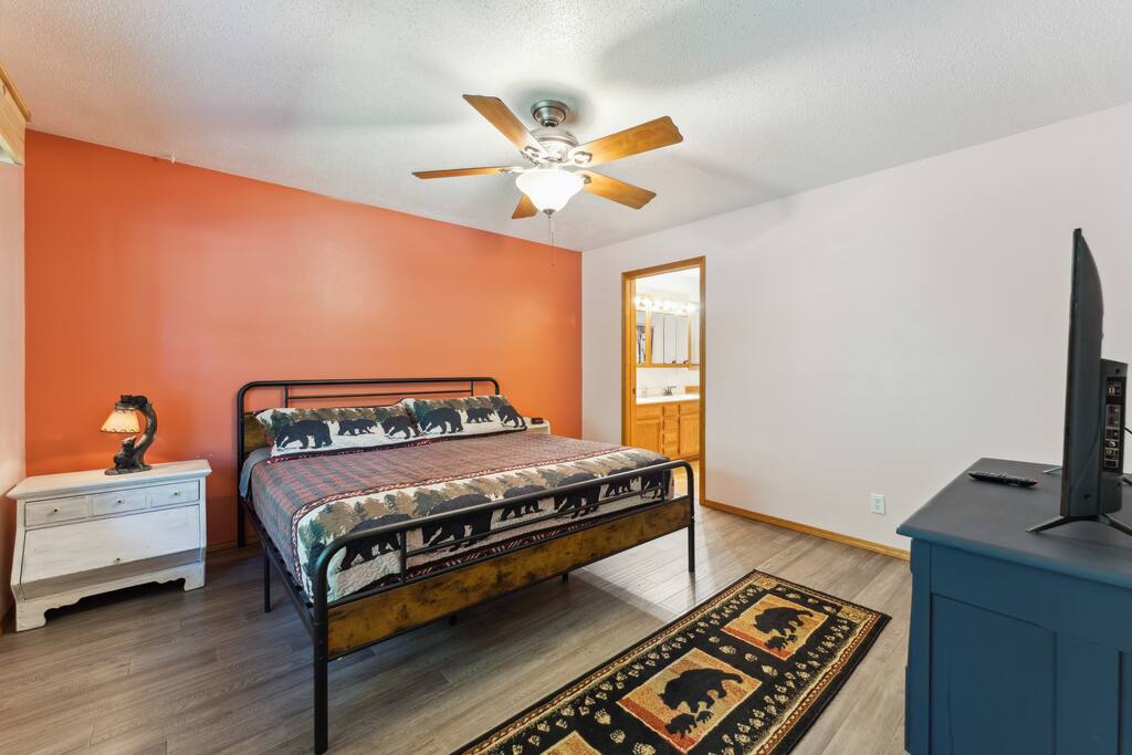 Master Suite Main Level Bedroom with a king bed, Roku TV, USB charging ports on lights, dresser, closet with hangers, master bathroom connected to the bedroom with tub/shower, hairdryer, and iron/ironing board. Master Suite Main Level Bedroom with a king bed, Roku TV, USB charging ports on lights, dresser, closet with hangers, master bathroom connected to the bedroom with tub/shower, hairdryer, and iron/ironing board. - Bear Cove Escape - Lyndon Station