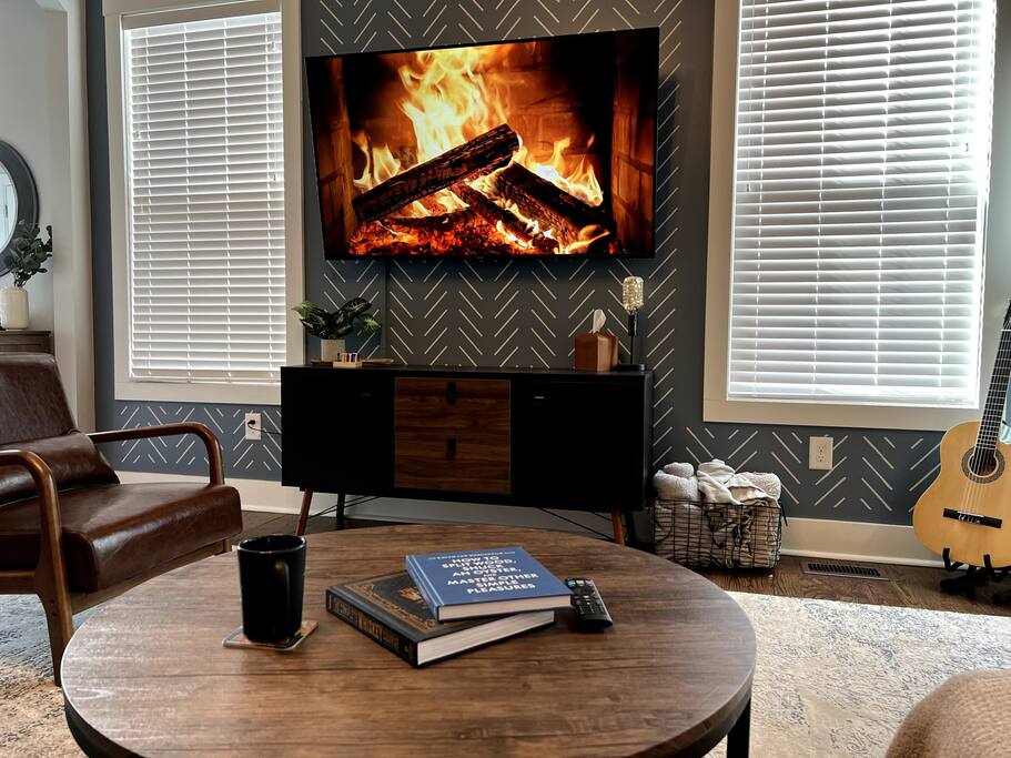 Living room with POV from the couch showing wall mounted 65" Vizio SmartTV, and coffee table books, throw blankets and acoustic guitar